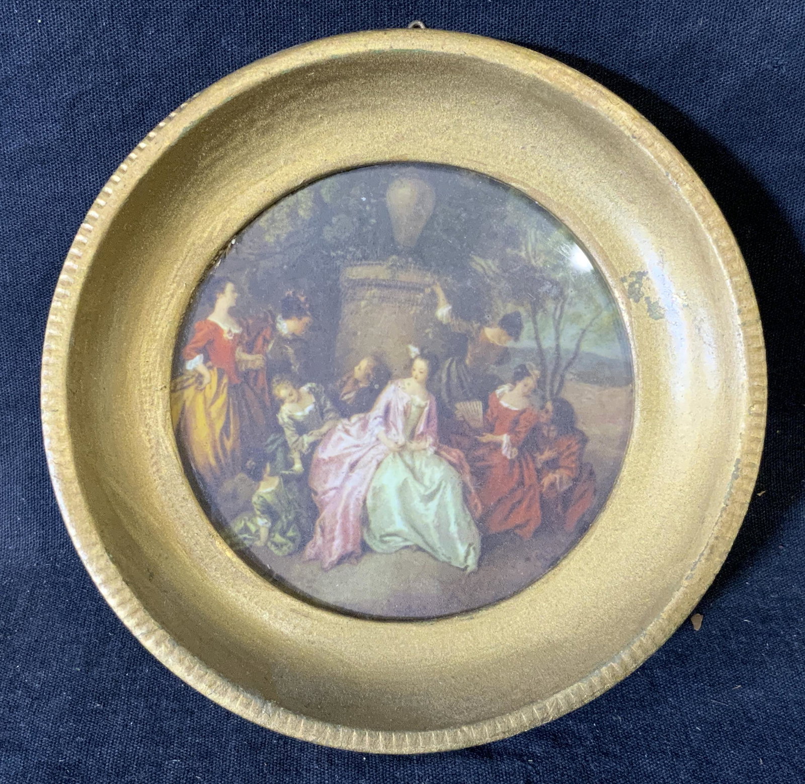 French Rococo Style Offset Lithograph, Artwork: French rococo style offset lithograph, no apparent inscriptions or markings, subject a group of women in Rococo dresses in a garden, gold painted wooden frame, circular frame, frame measures 5 inches 