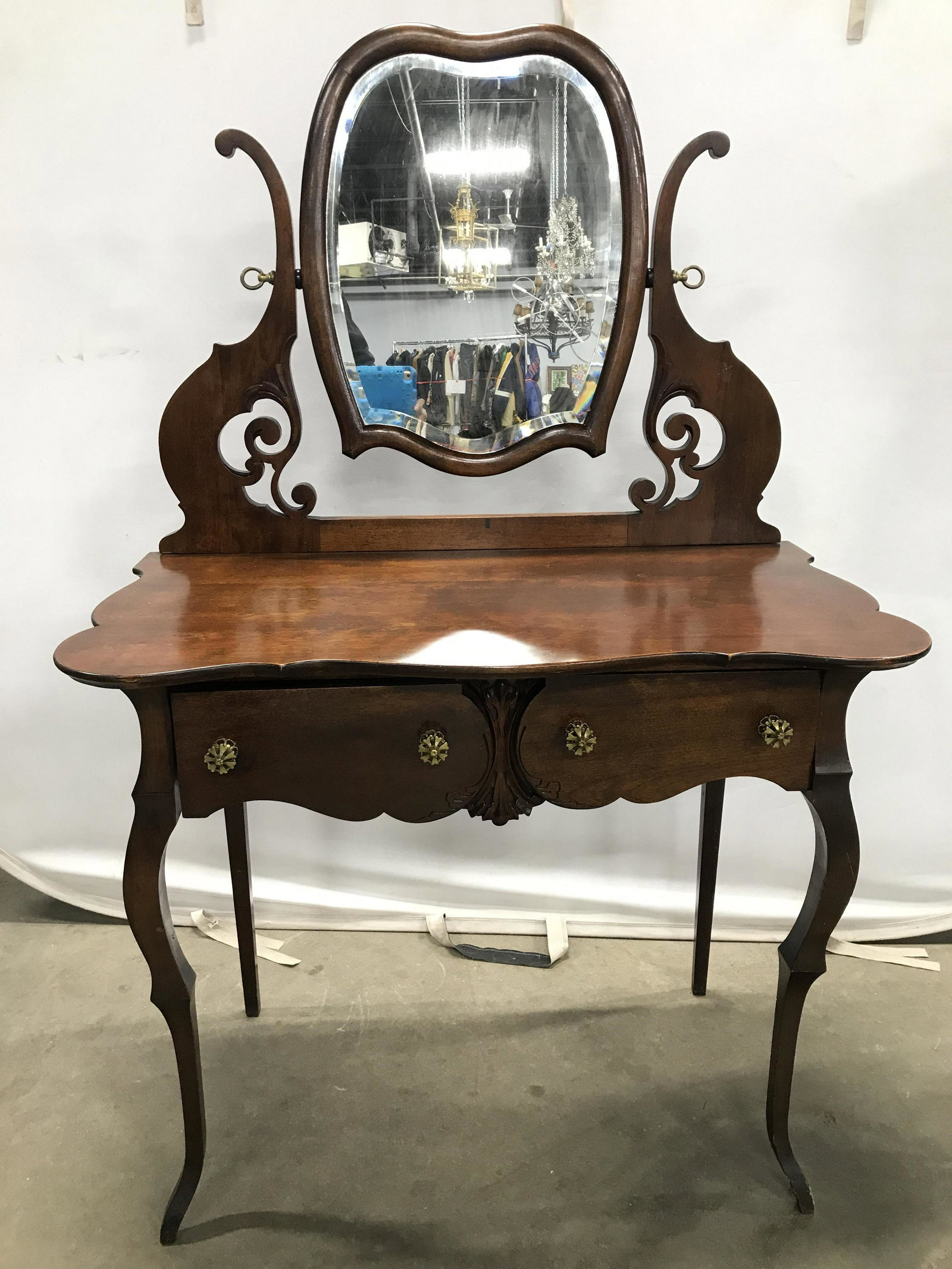 Vintage Wooden Vanity Table W Drawers: Vanity table is Brown toned & wooden, appears to possibly be vintage. Piece has 2 drawers each with gold toned metal knobs. Mirror supports have carved detail & May be hand crafted. Piece measures app