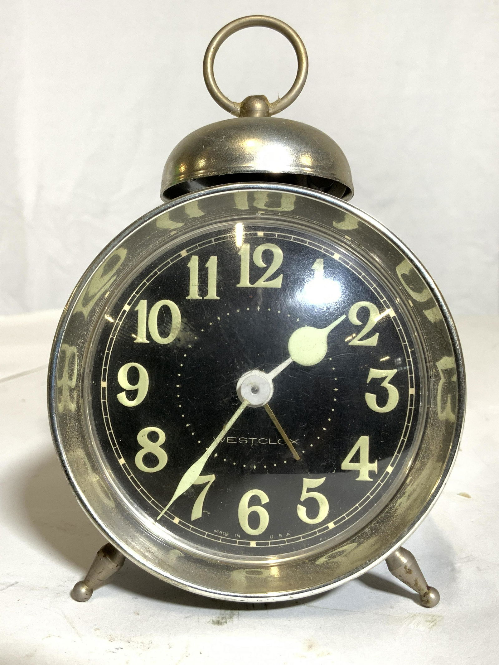 WESTCLOX Vintage Footed Alarm Clock: Clock face reads WESTCLOX. Piece has black clock face & backside. Piece has silver toned metal bell on top. Piece also has 2 Metal feet. Clock has seafoam green numbers & hands. Piece measures approx