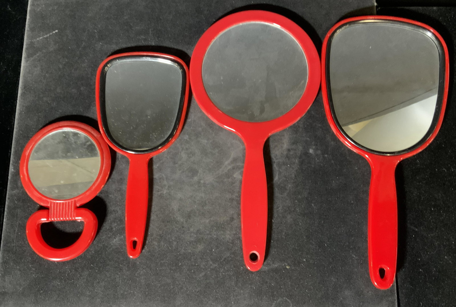 Lot 4 Handheld Red Mirrors: Four red mirrors, possibly vintage. Circular and square in form. Handheld. Various sizes. Largest Approx. 11 x 5 in. Three undersides have unique swirl designs. Property of multigenerational Brooklyn 