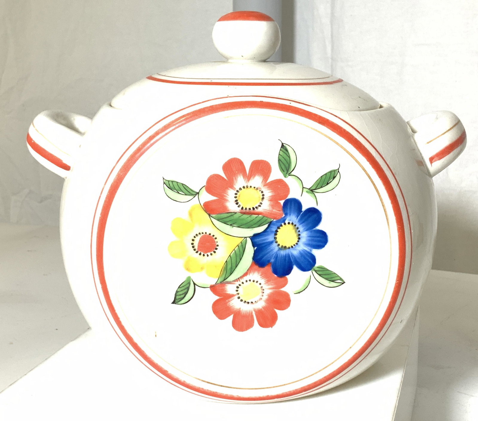 Vintage Ceramic Lidded Cookie Jar w Flowers, Japan: Ceramic Lidded jar with home country flair, vintage item painted bright red accents and yellow, blue & red flowers. Marked Japan P on underside. Glaze crazing. 9.5 in. L, 7.5 in. Ht. Property of Multi