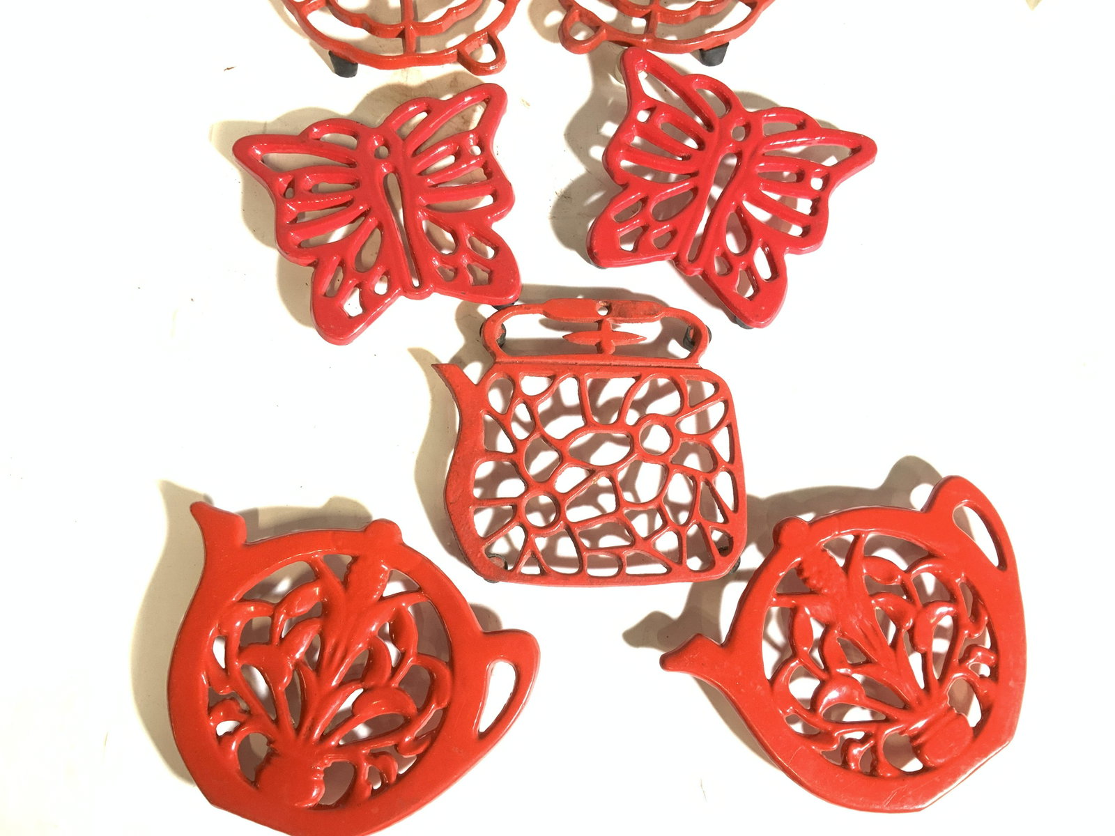 Group 7 Cast Iron Red Enamel Table Trivets: Collection of table trivets, a pair of butterfly form, pair of flower form, pair of teapot form ( 7.5 in. W) and additional teapot form. All have rubber feet. Property of Multi generation Brooklyn Col