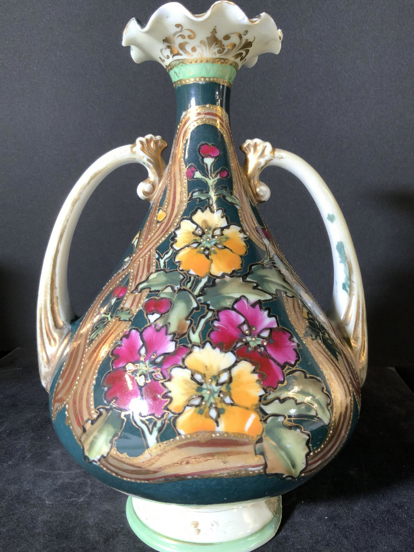 Hand Painted Ruffled Floral Porcelain Vessel: A white porcelain vase / vessel with twin handles. Decorated with hand painted florals and gilt line work. In relief accents along the center of the florals and gilt accents. Some chips and wear to pa