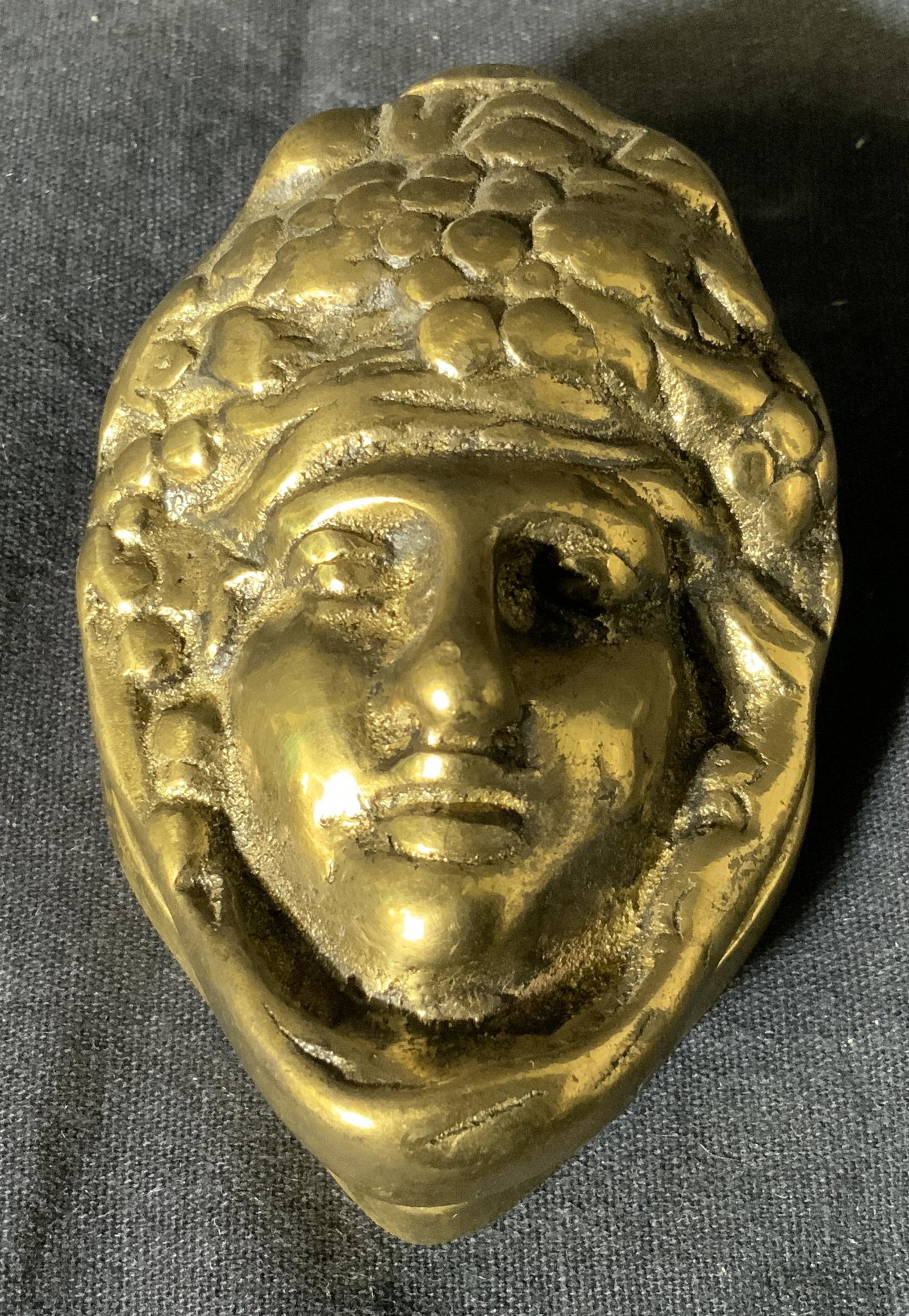 Brass Sculptural Relief Door Knocker: Brass sculptural relief door knocker, no apparent inscriptions or signatures, subject a relief of a face with fruit and flower surrounding it attached to a brass plaque for knocking, piece measures 3.
