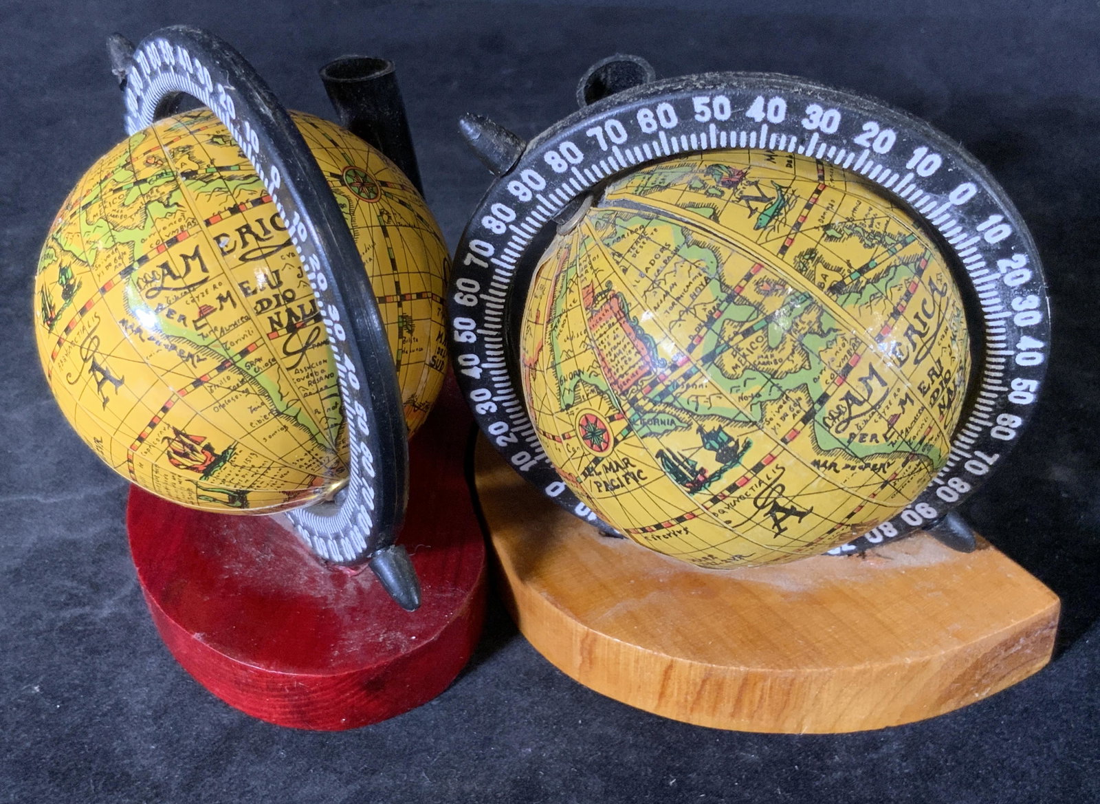 Pair Vintage Globe Desktop Pen Holders: Two vintage near pair desktop pen holders. Each pen holder is affixed to a wooden stand and adorned with a decorative globe accessory. The globes both spin. One globe’s paper has come loose. One bas