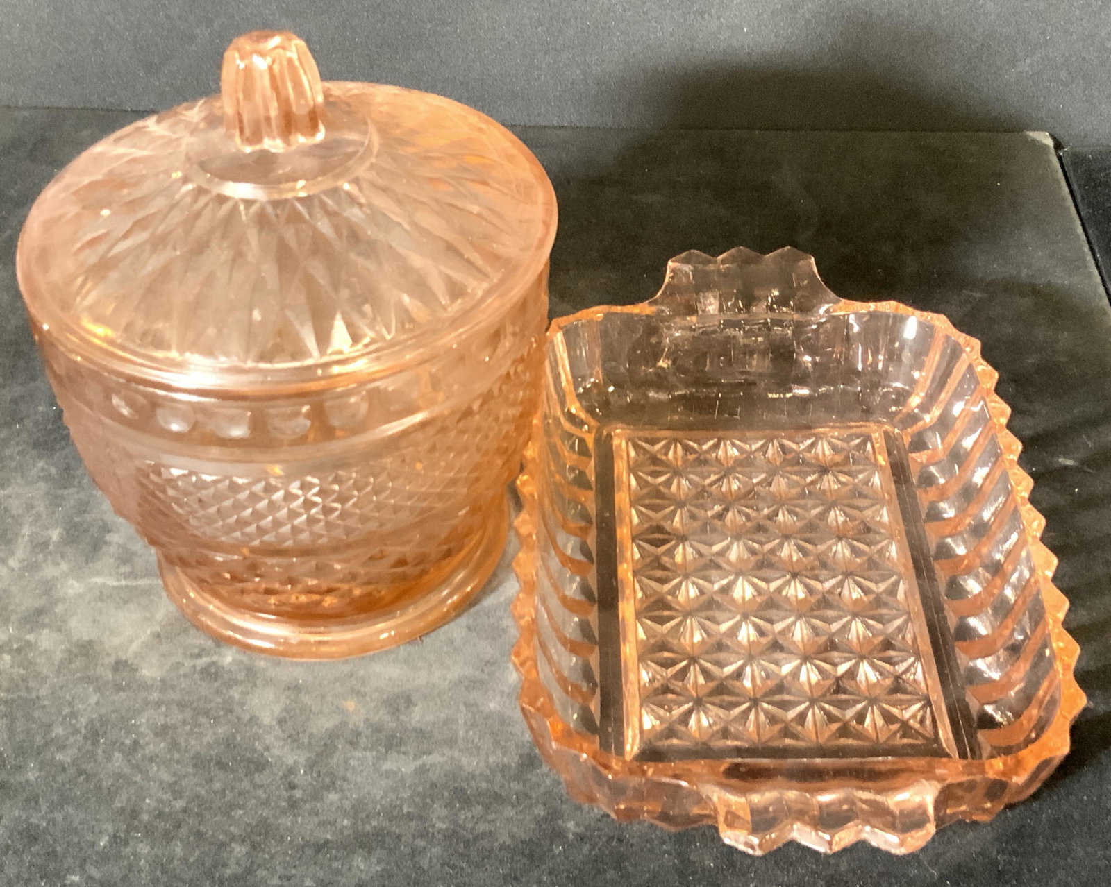 Lot 2 Pink Hued Molded Glass Accessories: Two pink hued molded glass accessories that can be used anywhere in your household. Pieces feature cut designs and pink hues throughout. One piece is a lidded vessel with a finial topper. Can be used 