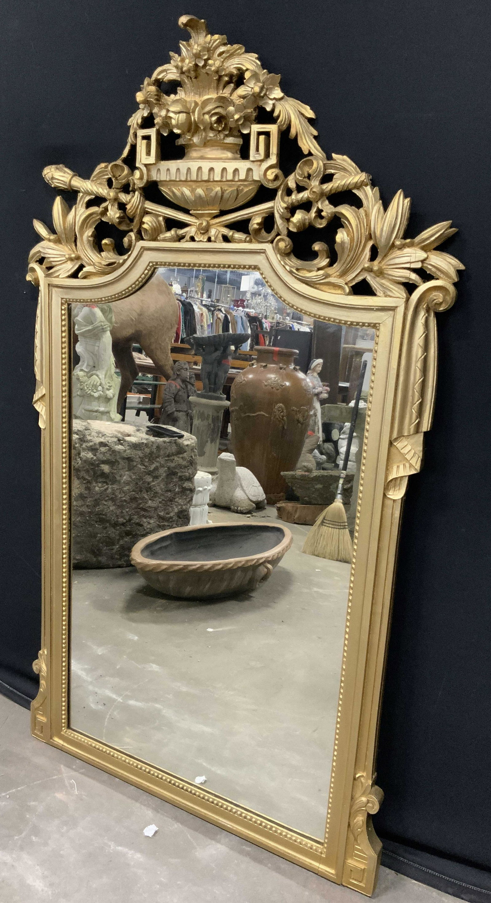 Vintage Gilt Wood Mirror: Vintage, possibly antique, gilt frame mirror. Frame is hand carved wood. Frame is hand painted and gold toned. Apex of mirror is decorated with a carved pedestal bowl, bowl holds flowers, two scepters