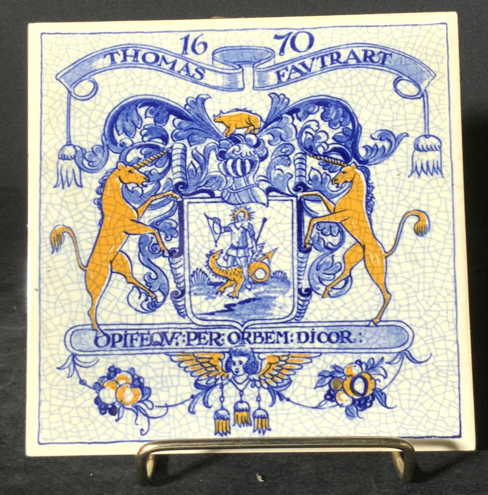 Signed Handmade Blue & White Ceramic Tile, Holland: A blue and white glazed ceramic tile depicting a crest like design. Piece is primarily blue and white with yellow accents. Unicorns, mythological creatures, a man, and an Angel are depicted on the cre