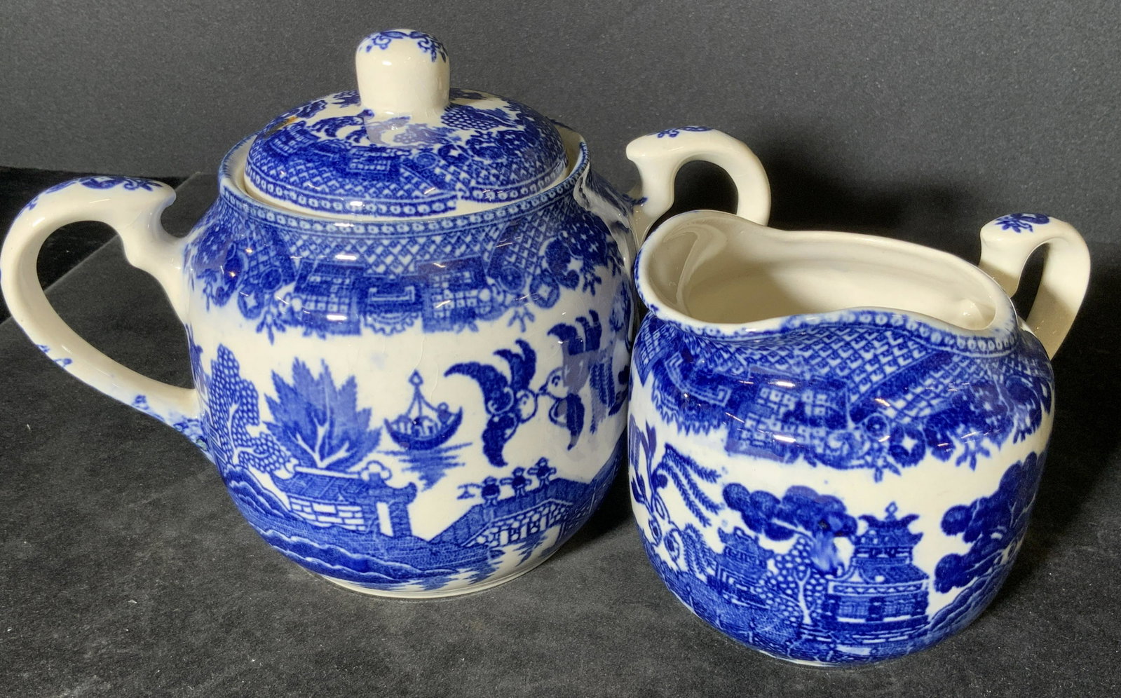 2pc Blue & White Asian Porcelain Tableware, Japan: Two blue and white collectible porcelain tableware accessories. One lidded vessel with twin handles. Piece can be used for storing sugar or other tea accessories, and more. Creamer vessel with one han