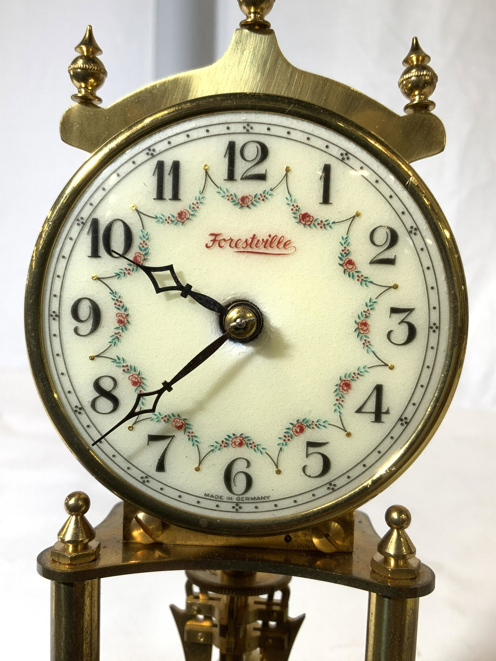 Vintage FORESTVILLE Footed Anniversary Clock: Clock face reads FORESTVILLE MADE IN GERMANY. Piece is gold toned with cream clock face & black numericals. Base has circular shape. Piece has 4 gold toned spinning spherical structures. Clock is foot