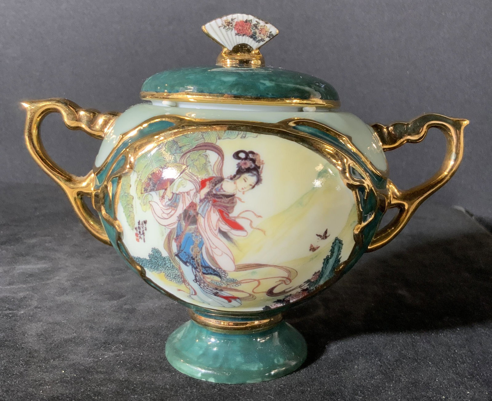 C. 1991 ARDLEIGH ELLIOT Porcelain Music Vessel: A lidded porcelain vessel with twin handles. The piece is decorated with Asian style motifs. A woman walks elegantly through a nature scene in traditional clothing. She holds a fan. There are Asian ch