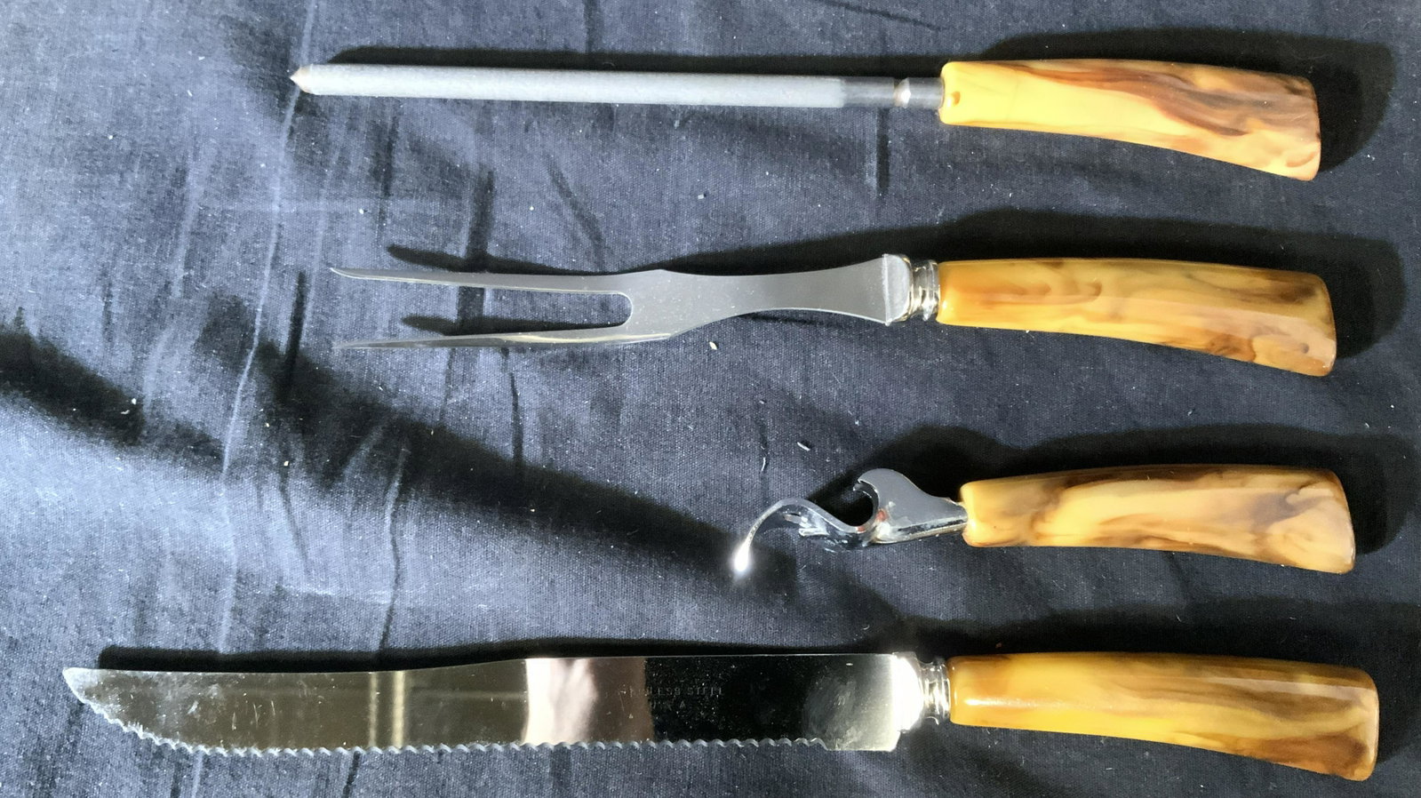Set 4 Vintage Steel & Bakelite Kitchen Accessories: Set of four vintage kitchen accessories. Includes a carving knife & fork, a bottle opener, and a knife sharpener. Handles are Bakelite, knife and fork are marked: stainless USA. Largest piece measures
