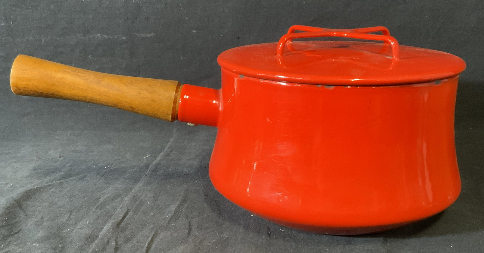 DANSK Kobenstyle Saucepan: DANSK saucepan, possibly vintage. Crimson toned, handle is wooden. Includes a lid, handle is x-shaped. Measures approx 5.5 inches H, and 14 inches W. Wear is consistent with use. Property of a multige