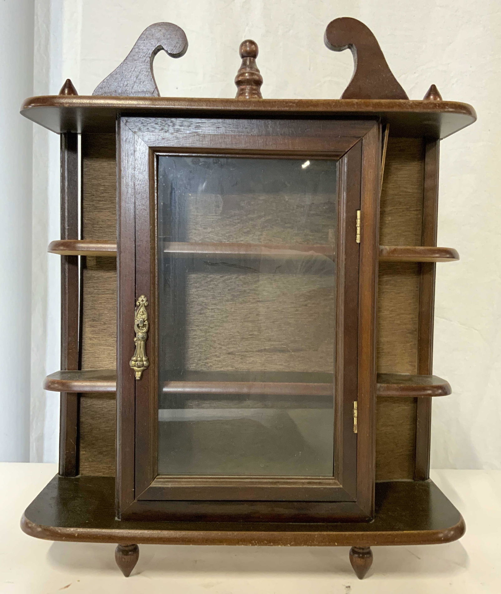 Vintage Windowed Wall Curio Cabinet Shelf: Wall curio is vintage. Piece appears to be wooden possibly veneer. Piece has 2 shelves & 1 windowed cabinet door. Piece has carved finial detail. Piece measures approx 17 inches tall 14 inches wide 4 