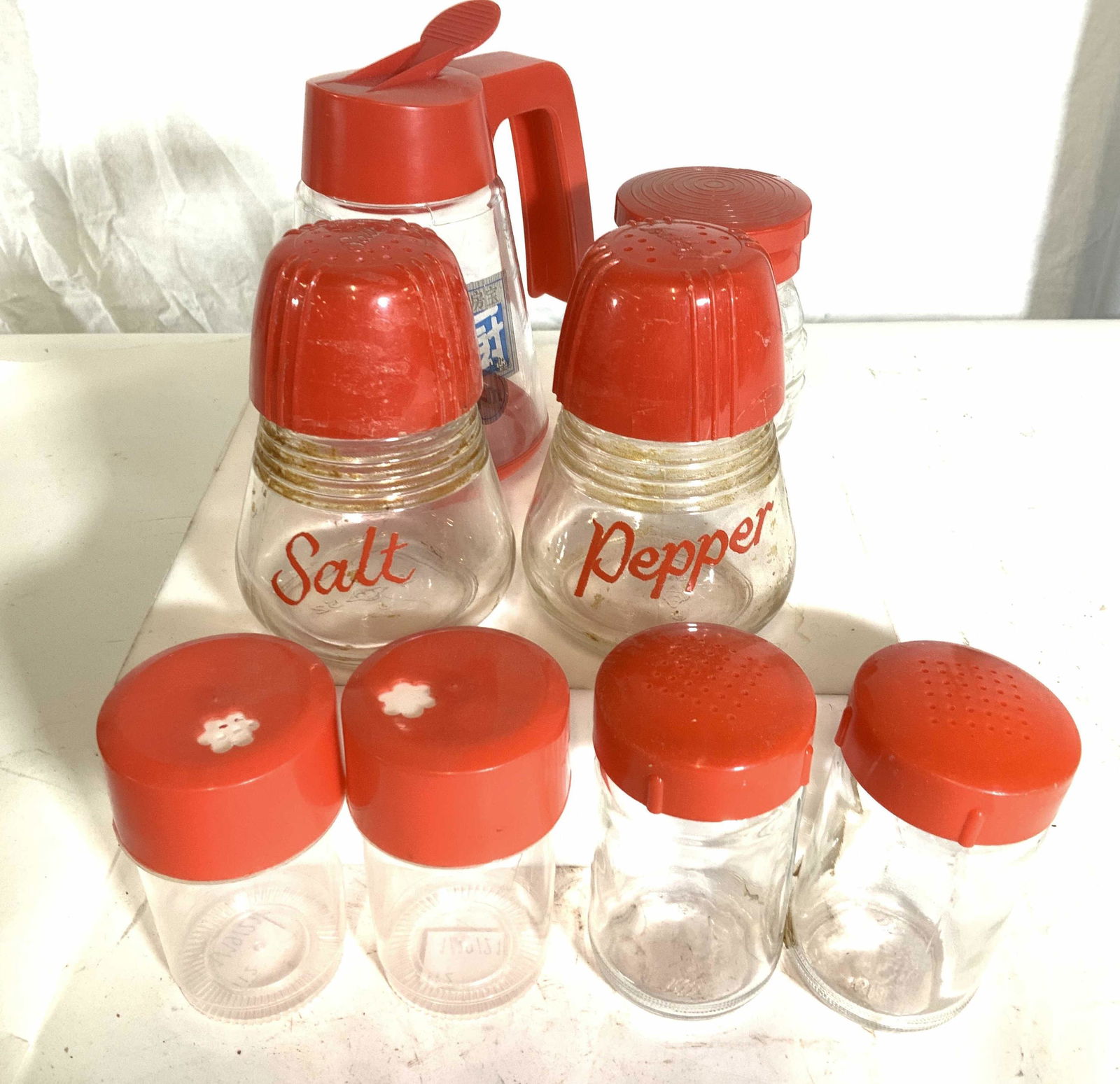Group 8 Red Kichenalia Table Accessories: Lot consists of a plastic syrup pourer, glass salt and pepper shaker, embossed glass spice shaker, pair plastic shakers, pair of glass shakers. Property of Multi Generation Brooklyn Collector’s Esta