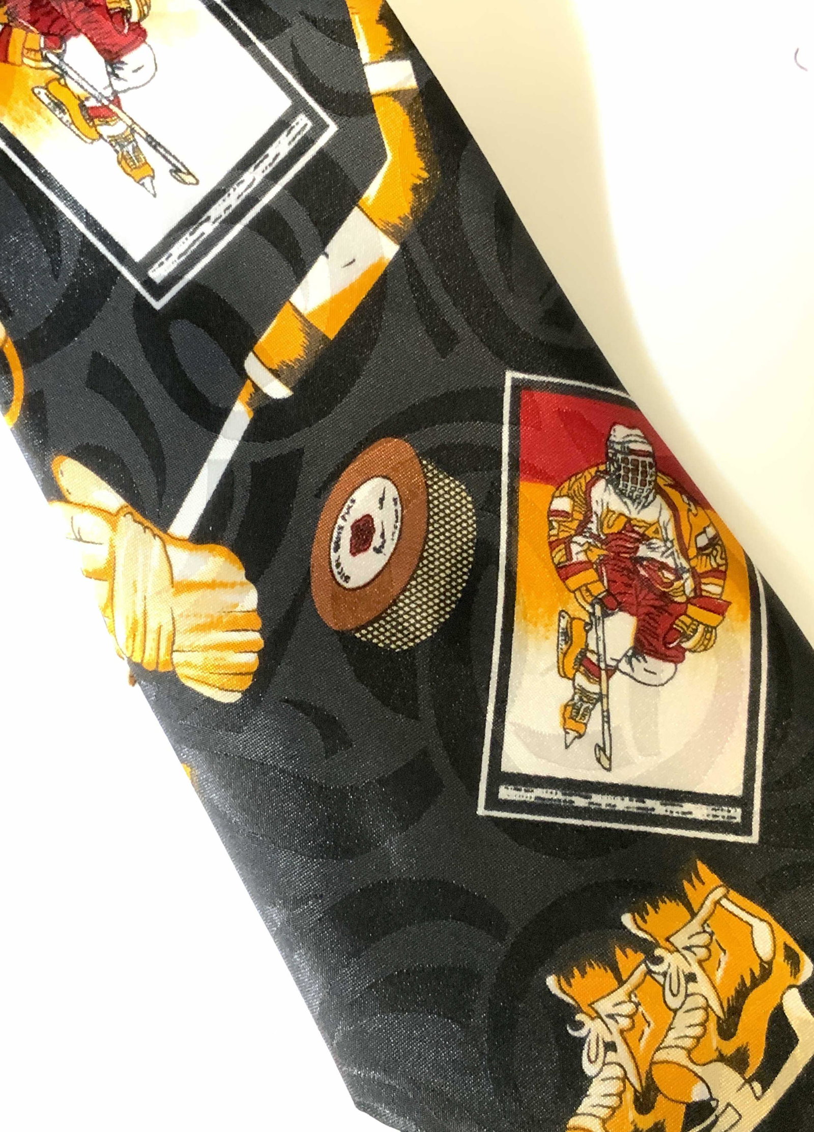 DINO ROMARO HANDMADE Ice Hockey Neck Tie: Fun fashion tie. Designer label reads Dino Romaro in gold thread, also reads Hand Made. Black with colorful depictions of ice hockey player. Made of silk. Has label that reads Trade Silk Co. Wide widt