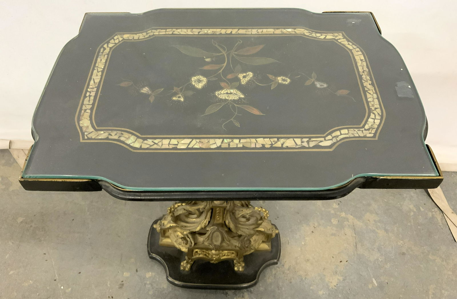 Vintage Ornate Side Table W Mother Of Pearl Inlay: Side table is vintage possibly antique. Piece has intricate ornate base with gold toned brass lion head structures, paw feet, leaf, c and s scroll detail. Piece has glass top. Table top has mother of