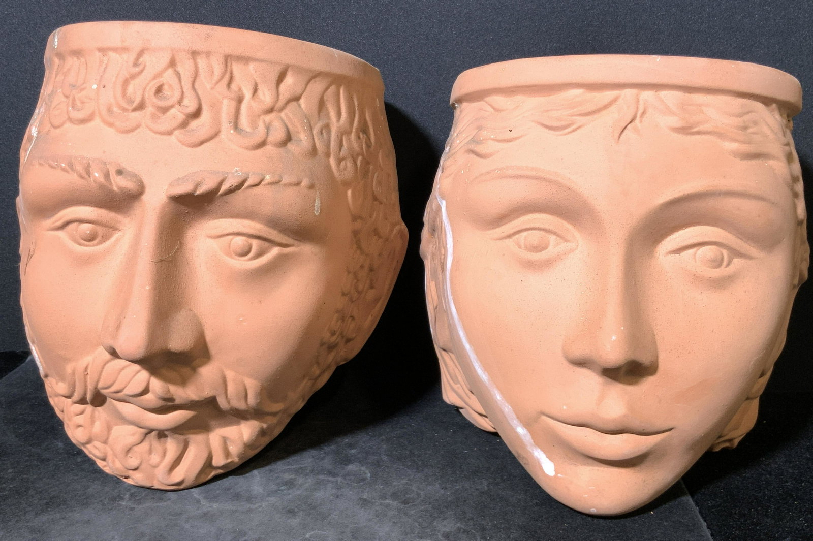 Pair Male & Female Terracotta Hanging Planters: Two terracotta hanging planters. Carved and embossed terracotta give each piece a realistic quality. One planter depicts a man with a beard & curly hair. The other depicts a woman with short, wavy hai