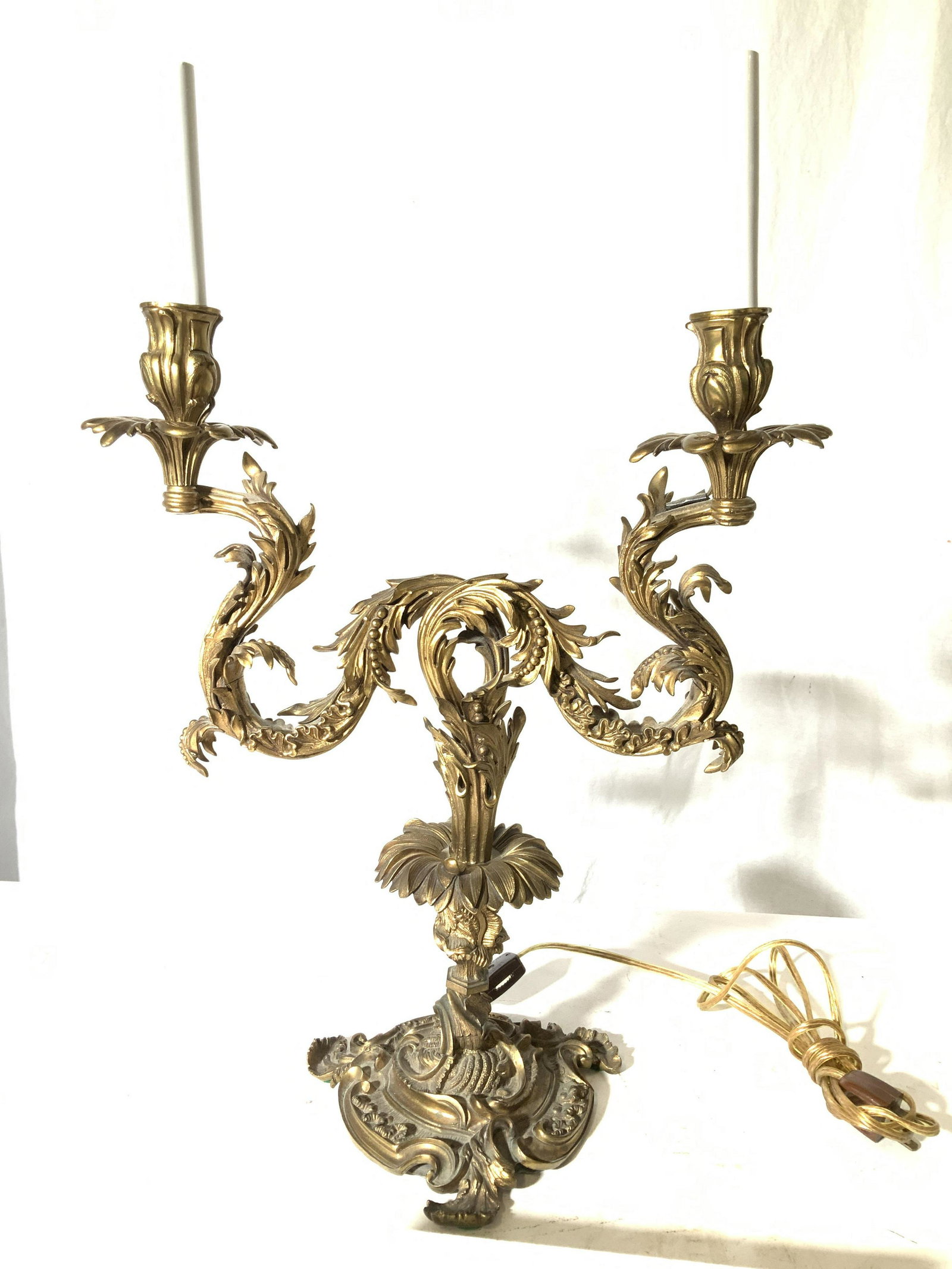 Gilt Bronze Baroque Duex Chandelier Table Lamp: Vintage baroque/ rococo gilt bronze lamp with two candle chandelier lights on each side. Laurel and berry decor, center stem daisy flower, felt under bronze to protect furniture, light switch on long 
