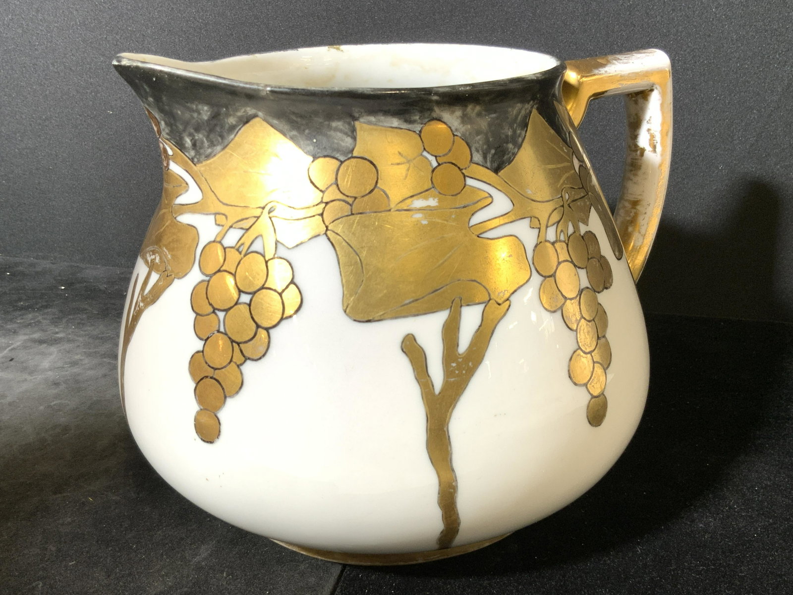 H & C SELB Vintage Bavarian Porcelain Cider Jug: A white porcelain cider jug / stout pitcher decorated with hand painted black and gilt designs. Designs include grapes and grape vines along all sides. The handle is covered in gilt paint as well. The