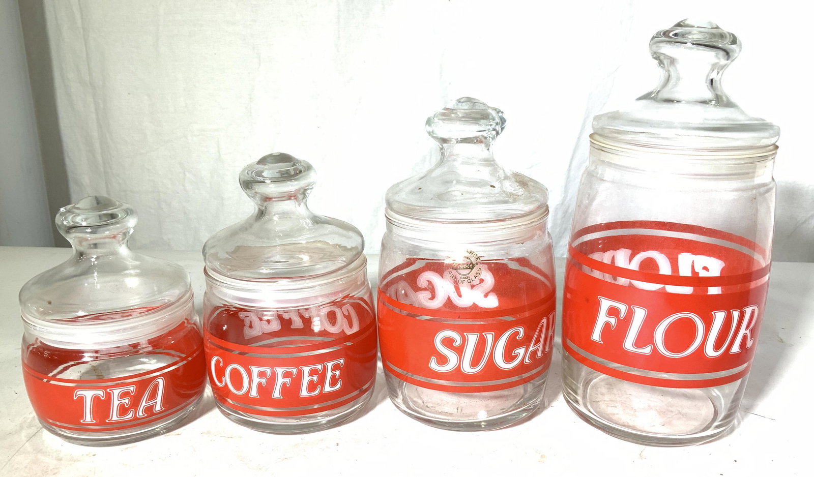 Set 4 Kitchen Countertop Lidded Canisters, Turkey: Glass canisters/ jars with rubber seal, one each for TEA BAGS, COFFEE, SUGAR & FLOUR. Tallest jar 9 x 4.5 in. Label on sugar jar reads Art of Glass Turkey Properly of Multi Generation Brooklyn Collect