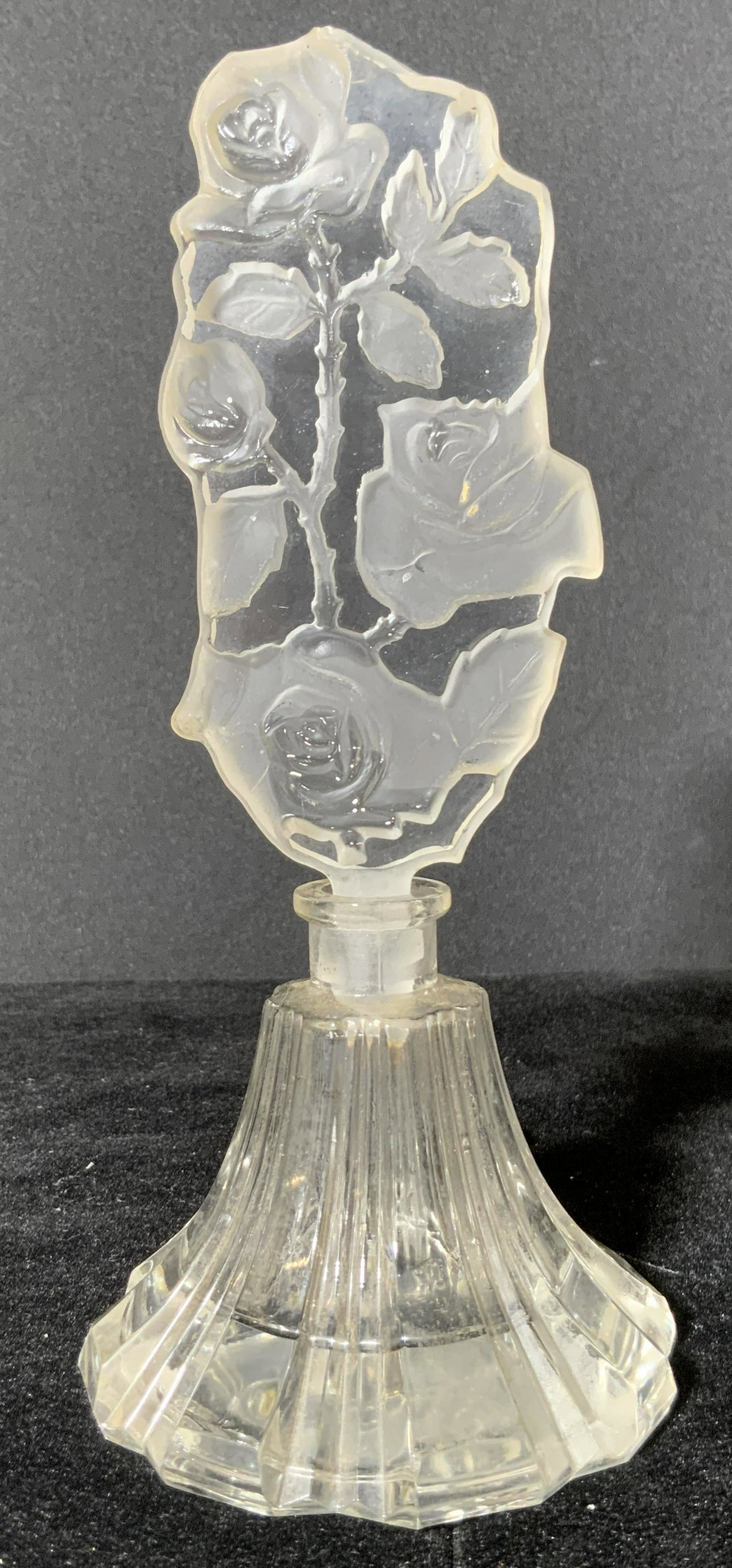 Vntg Carved & Etched Glass Perfume Bottle: A vintage colorless, transparent glass perfume bottle. The topper features carved & etched rose forms. The tip of the stopper is broken, it appears to be loose in the interior of the bottle. The base 