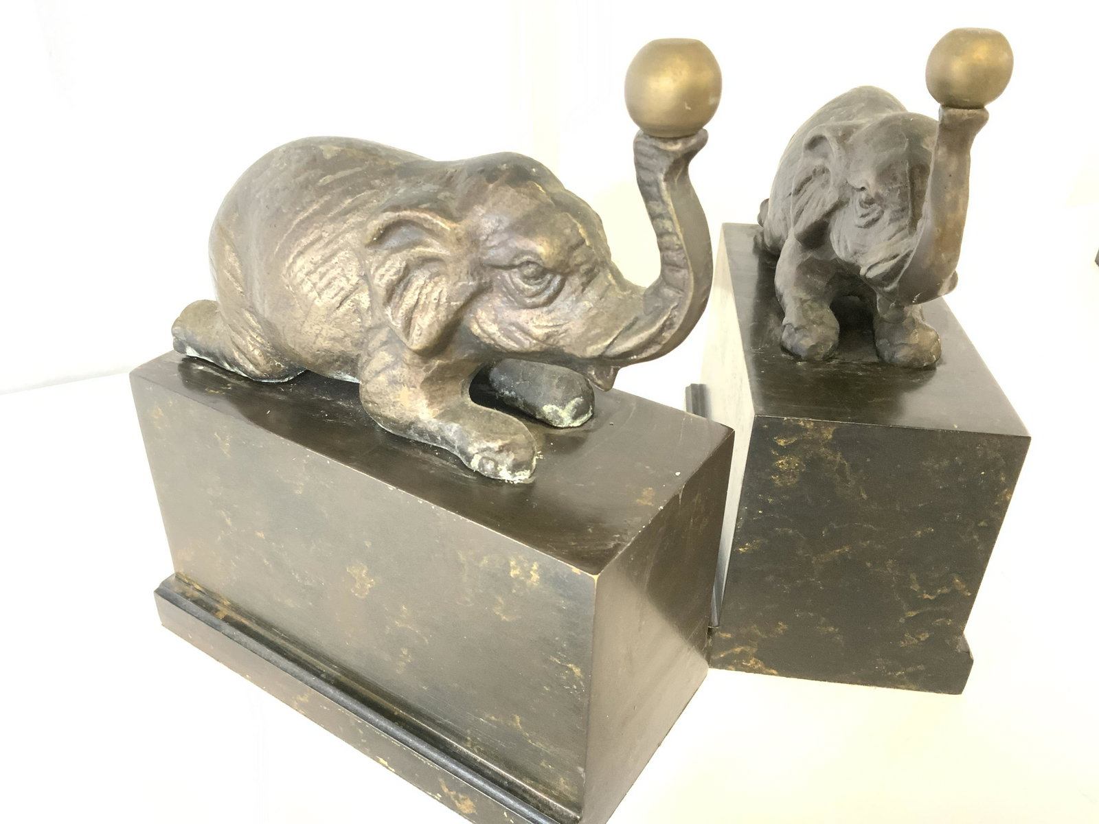 Pair BRONZE ELEPHANT Figural Statue, Korea: This pair of elephants is in a sitting position and playing with a ball using their trunk. They sit on a dark marbled laqueur Structure, underside of one has a sticker that reads Made in Korea. 6.75 i