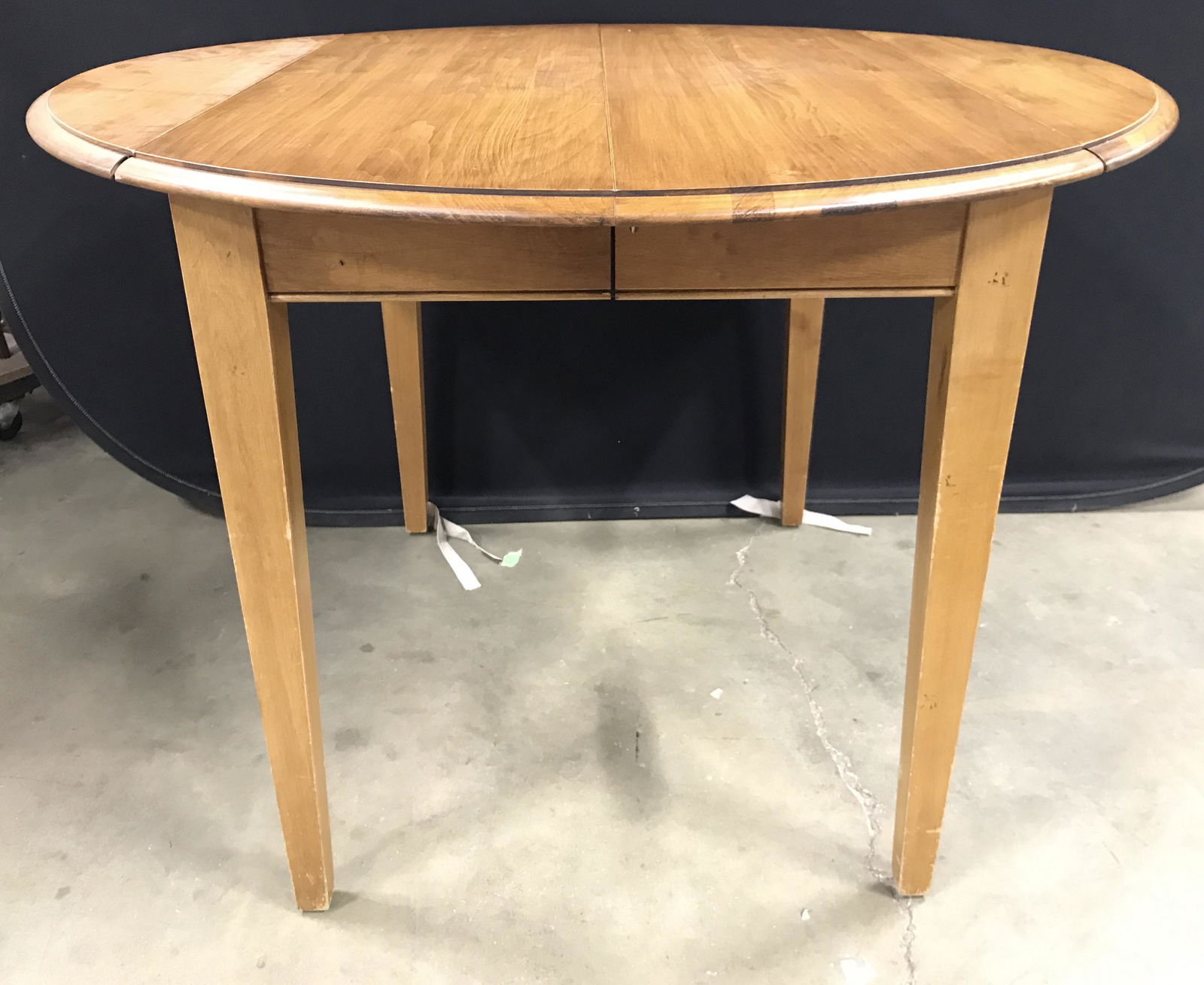 ETHAN ALLEN Mid Century Modern Dining Table: Underside has tag which reads ETHAN ALLEN. Dining Table is wooden. Table has 2 drop leafs. Piece opens in center to extend. Table has round shape. Table has 4 wooden legs. Dining table, Ethan Allen Ta