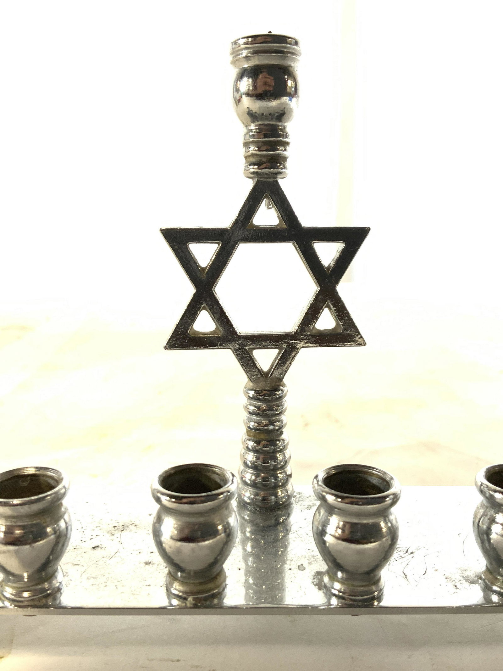 Footed Metal Menorah W Star Of David: Menorah appears to be vintage. Piece has Star of David structure in center. Menorah is silver toned and metal. Piece has 3 metal feet. Piece measures approx 8 inches long 4 inches tall 2 inches deep. 