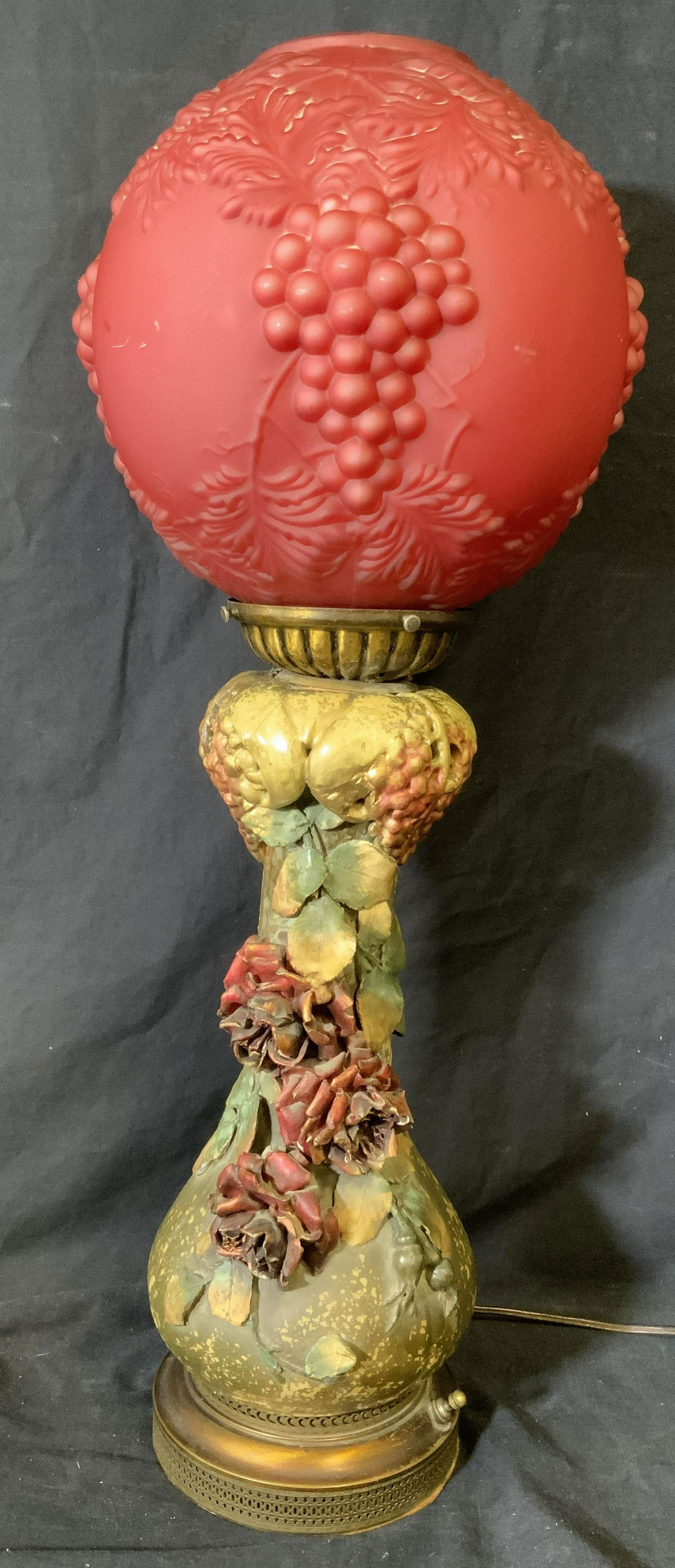 Ornate Rose & Grape Gone-with-the-Wind Lamp: Ornate rose and grape Gone-with-the-Wind Lamp, intake possibly antique, no apparent inscriptions or markings, lamp has a ceramic base with roses and grapes decorating the surface, bulbous red glass la