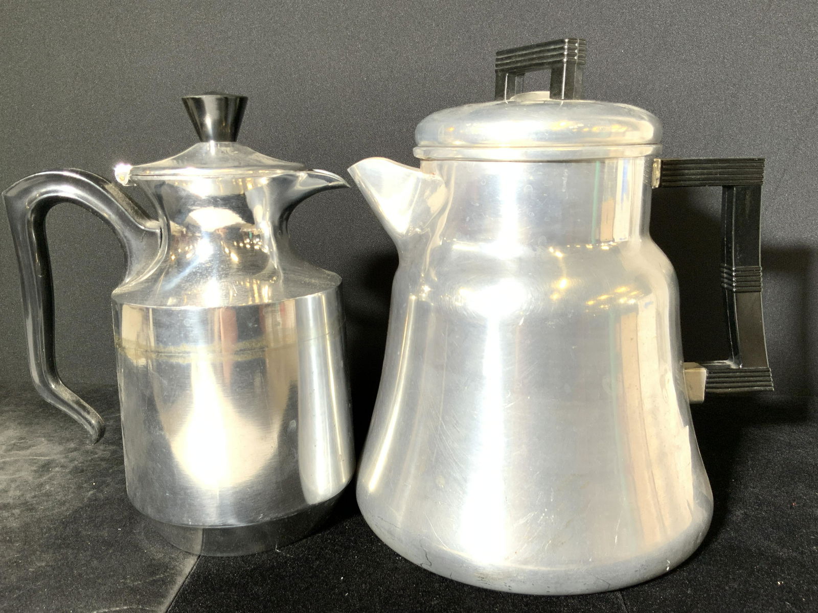 Lot 2 Vintage Aluminum Coffee Maker & Pitcher: Two vintage pieces of aluminum kitchenware. Both pieces are crafted from aluminum and have black composite handles and finials. One piece is used for making coffee. One piece has ash empty interior, l