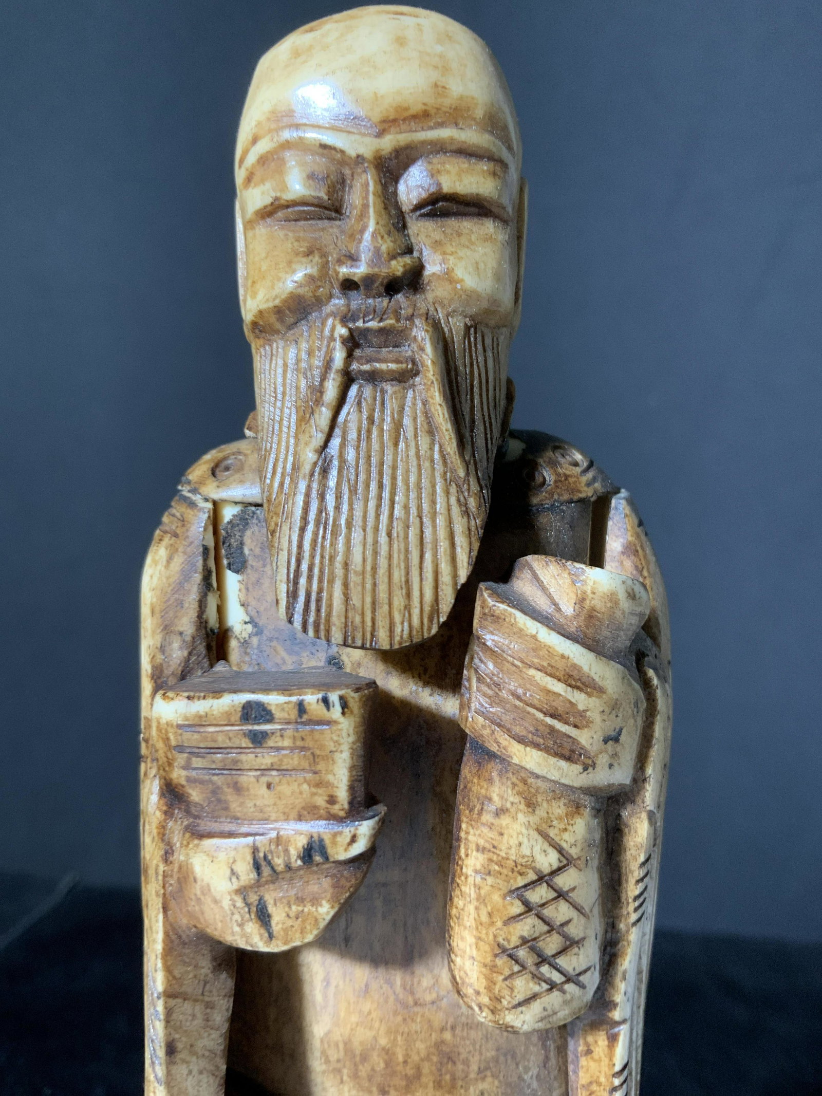 Collectible Vintage Hand Carved Asian Bone Figural: A vintage, possibly antique, Asian figural depicting a man holding onto two objects. Possibly depicting a bowl and a bag. The piece appears to be carved from bone. Precisely incised details throughout