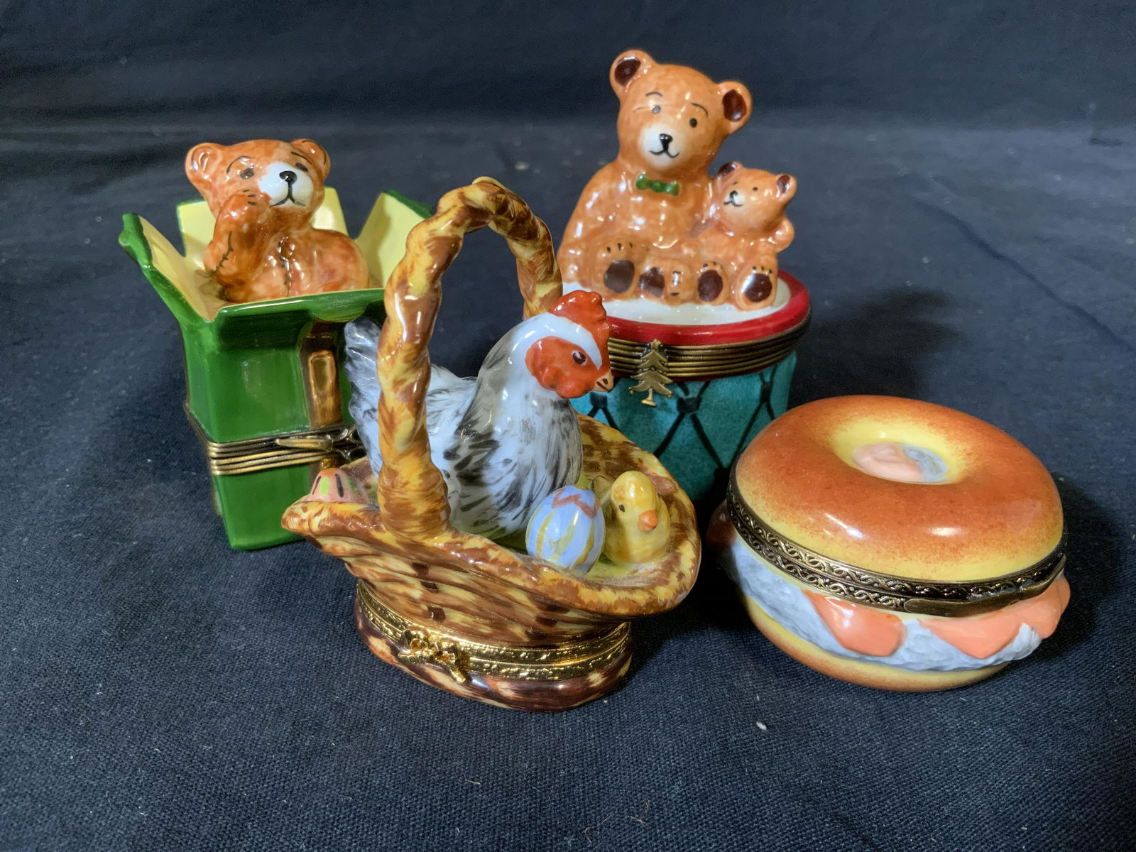 Group Lot 4 Porcelain trinket Boxes: Group lot 4 porcelain trinket boxes, three of four have an underside that reads ‘Limoges France’, box designs include a bear in a present box two bears on a drum a bagel sandwich and a basket with