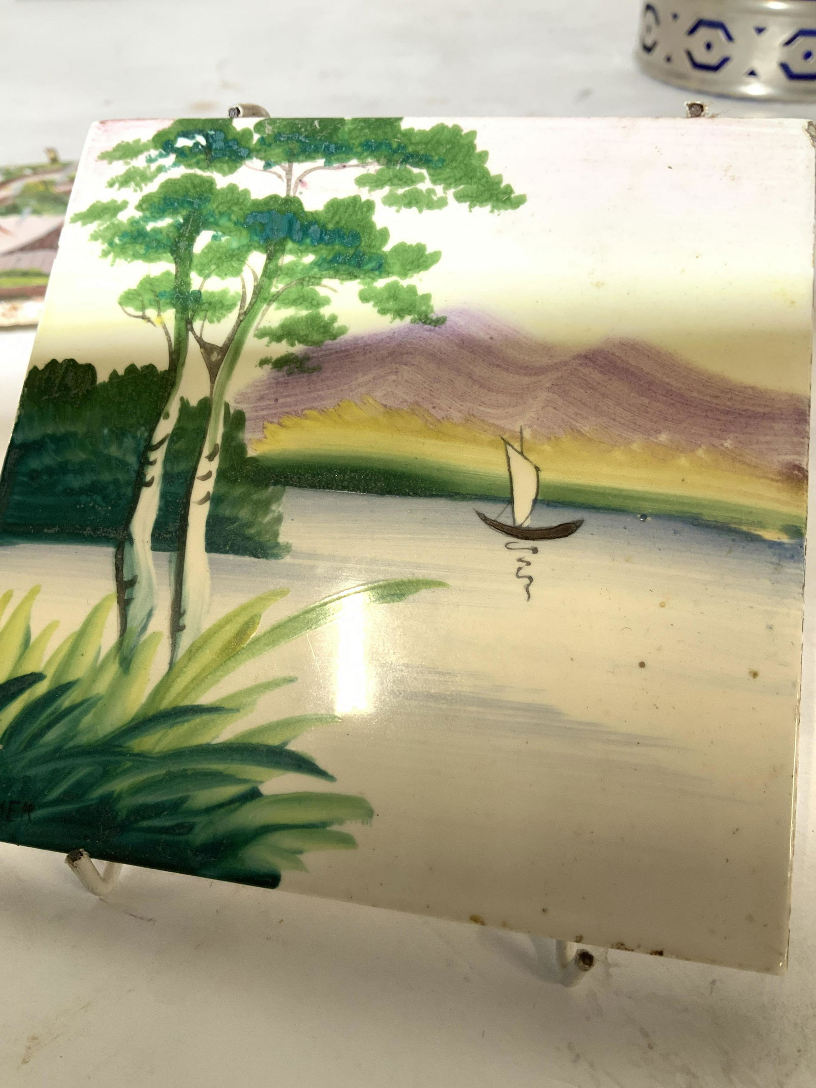 Lot 2 Hand Painted Ceramic Tiles, signed artist: Two hand painted tiles for wall decor, or can be incorporated into other design. One tile signed by artist, reads Rita Trosclair c. 1991. This tile has cracks that have been repaired, unglazed. Other