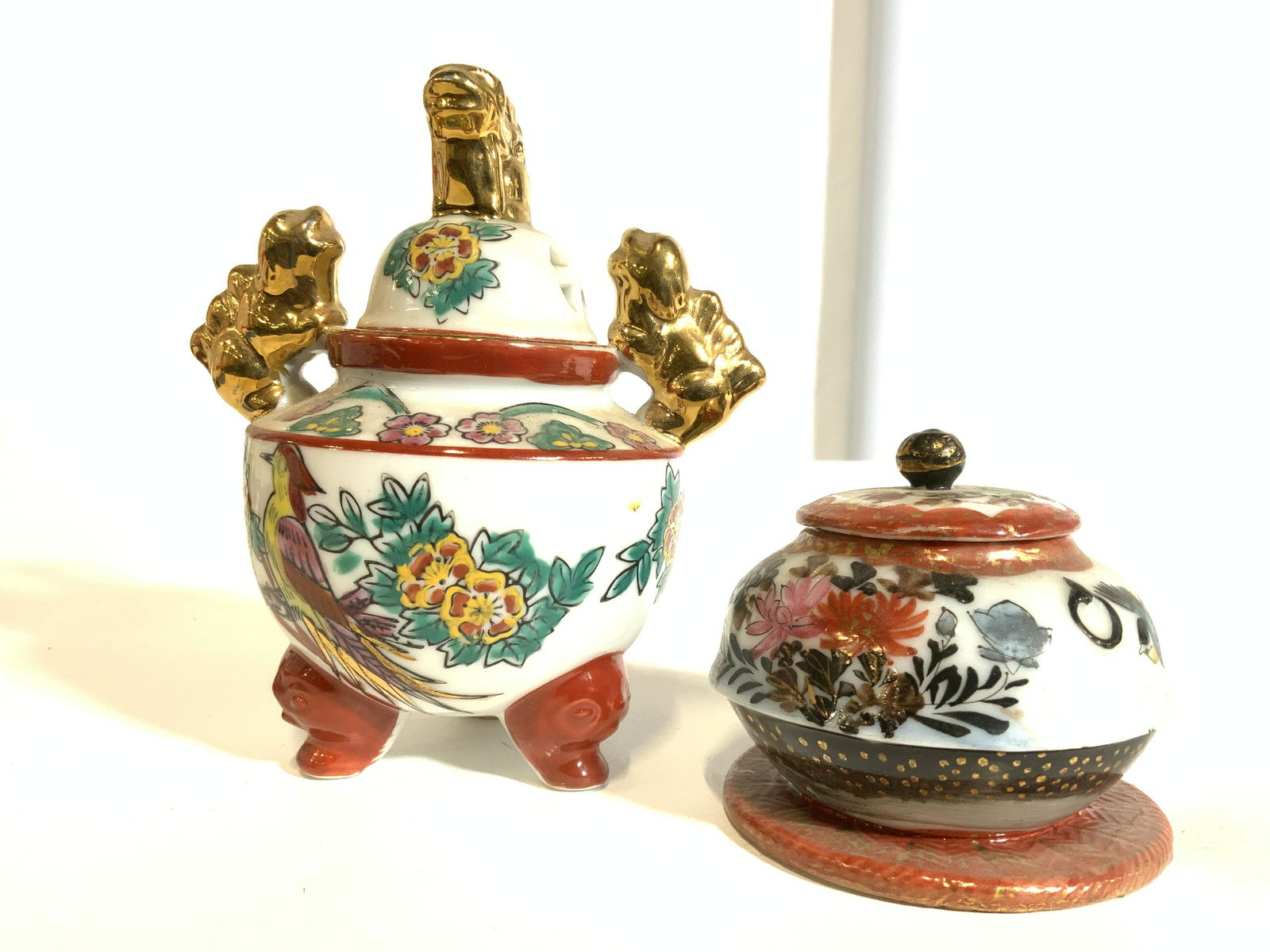Lot 2 Hand Painted Vintage Asian Porcelain: Lot includes 1 lidded vessel with feet & 1 lidded vessel with flat base. Each piece appears to be hand painted. One vessel has 3 red feet & 3 gold toned foo dog figurals at top. Painted detail depicts