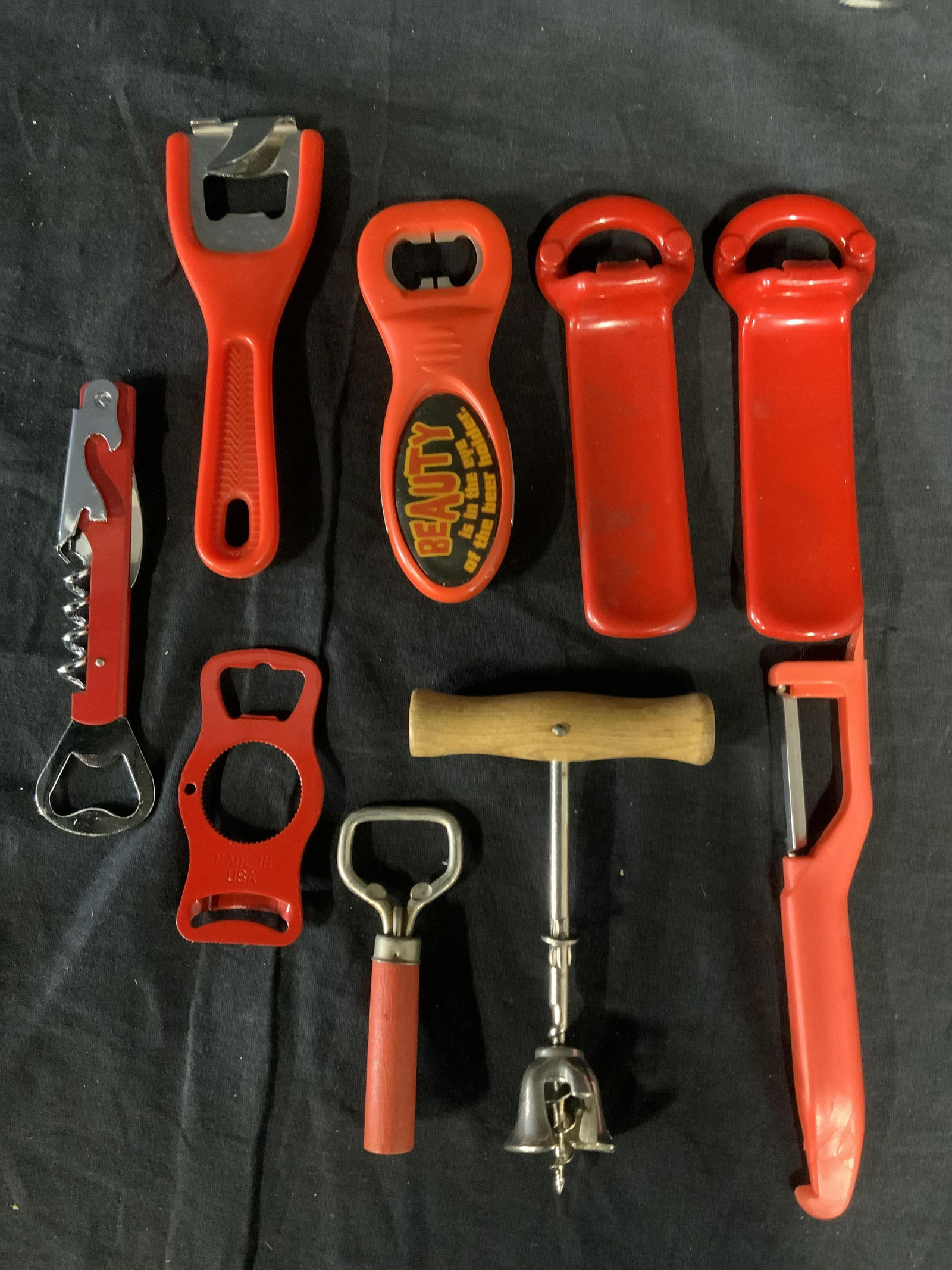 Lot 9 Vintage Bottle Openers, Corkscrews & Others: Items are vintage. Lot includes 2 corkscrews, one of which has bottle openers and a blade built in, 6 bottle openers, and a peeler. Several are orange/red-orange in tone. Largest piece measures approx
