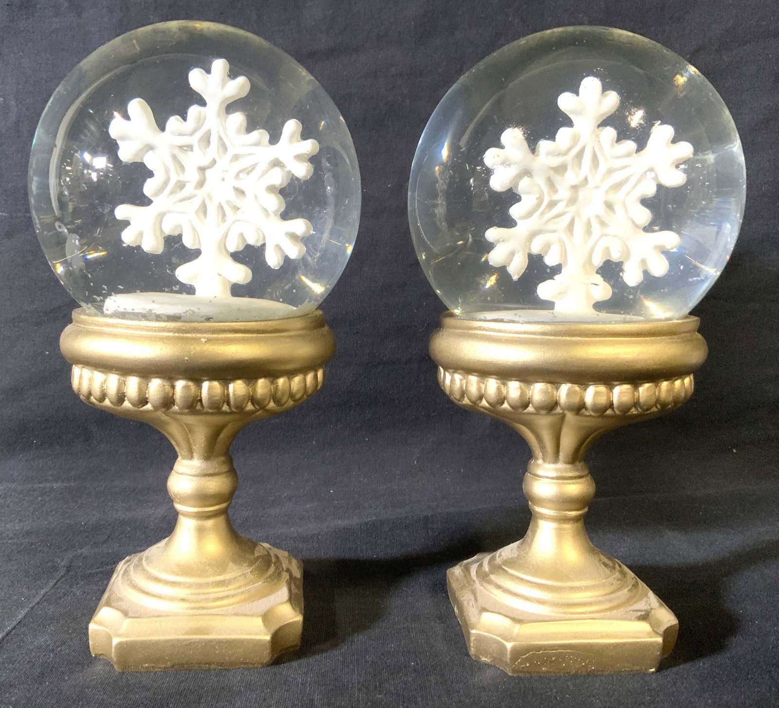 Pr Pedestaled Snow Globes W Snowflake Form Inside: Lot includes 2 snow globes. Each have gold toned pedestals. Interior of each piece has snowflake form. Each measures approx 7.5 inches tall 4 inches wide. Snow globes, pedestaled snow globes, pair of 