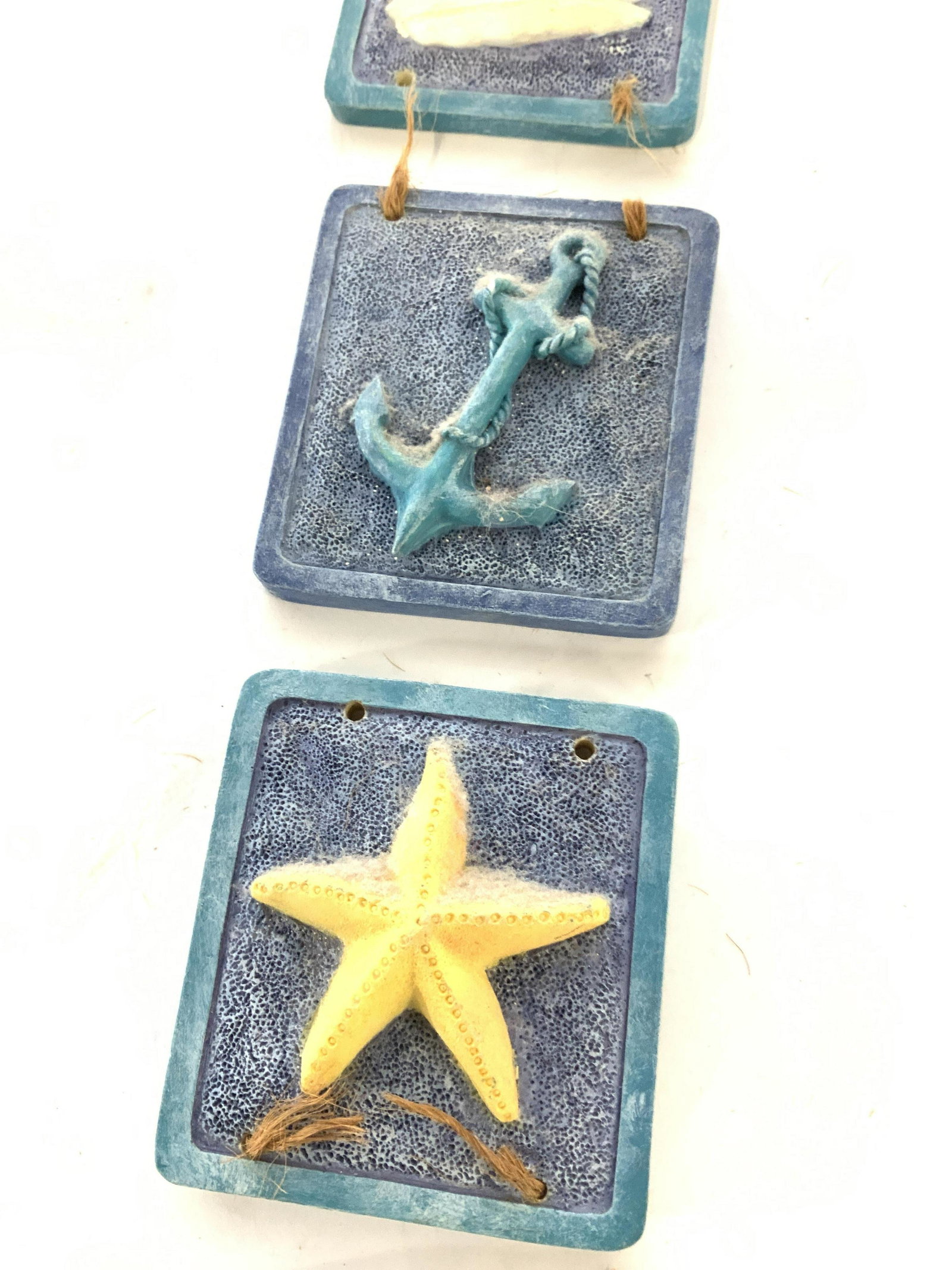 Maritime Ceramic Wall Decor & Magnets, 3: Two sailboat refrigerator magnets and one 4 piece tile wall decor, needs to be re- strung. Images include starfish, shark, anchor, and sailboat. Originally strung with raffia, can be used with any mat