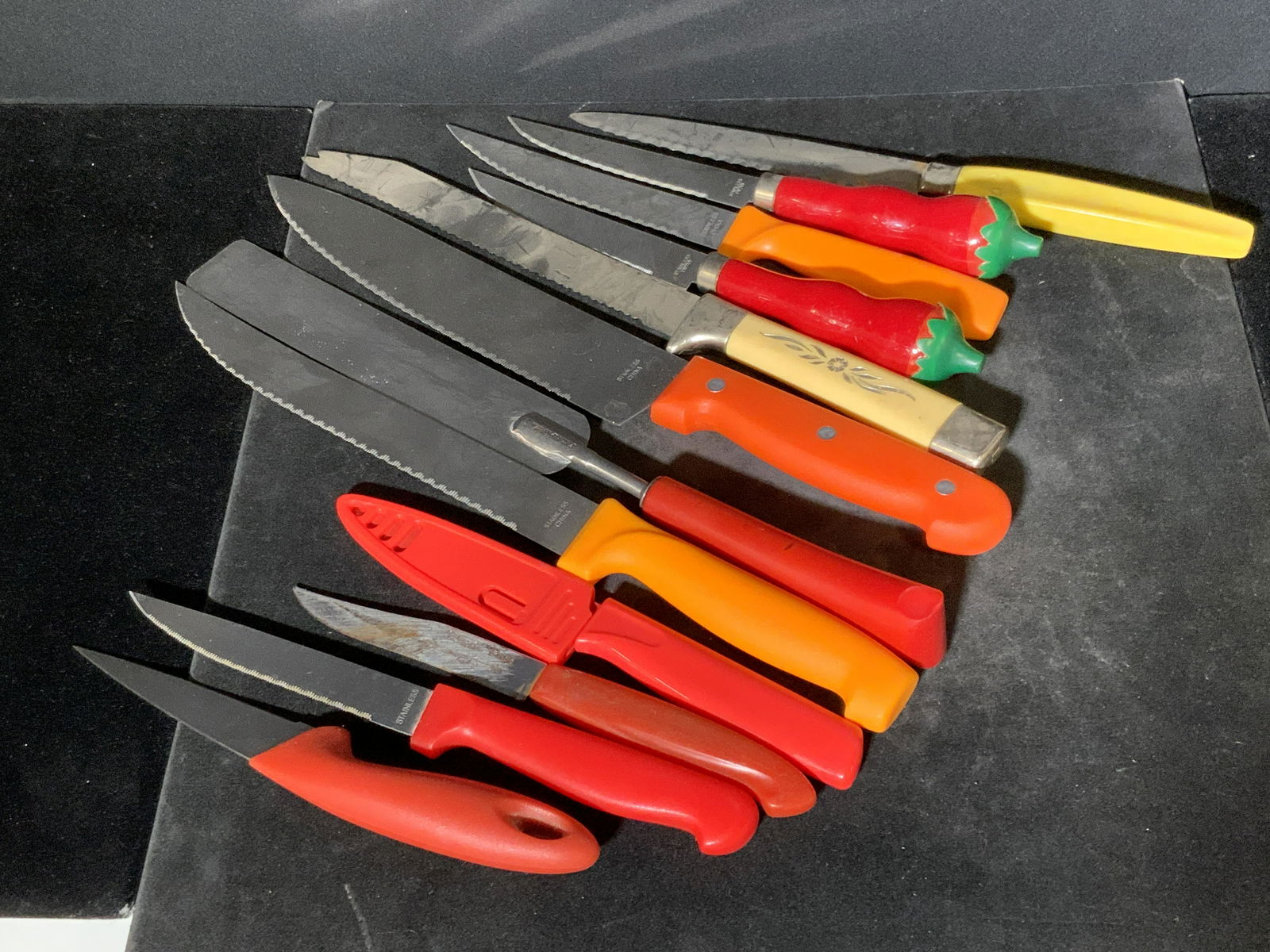 Lot 12 Vintage Kitchen Utensils, Knives & More: 11 knives and one flat serving utensil. Pieces are crafted from metals and plastics. Some knives are crafted from stainless steel. Largest Approx. 12L x 1.5W in. Property of Multi Generational Brookly