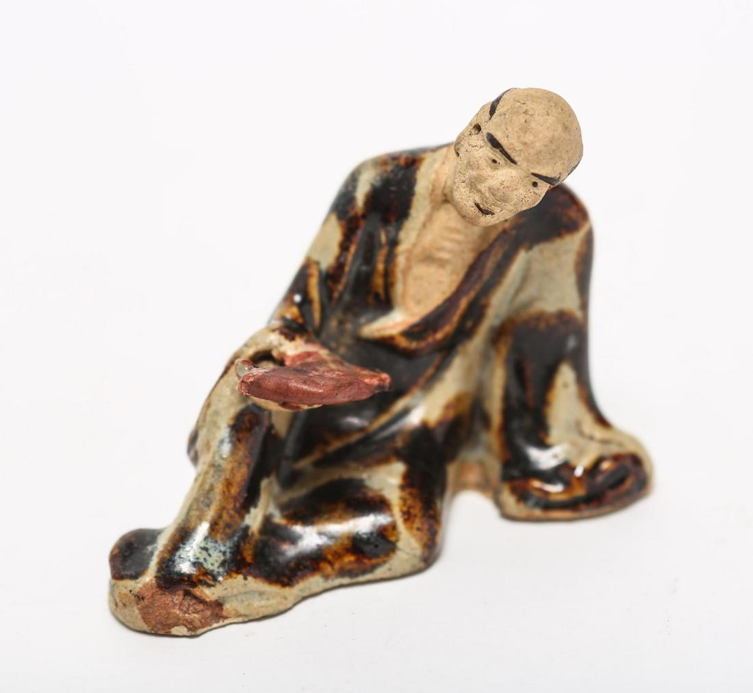 Japanese Lounging Man Ceramic Figurine Sculpture: Japanese Lounging Man Ceramic Figurine Sculpture Japanese ceramic figurine, depicting a robed man lounging with book in brown glaze. 2.75" H X 3.25" W X 1.75" D. Repair to neck.