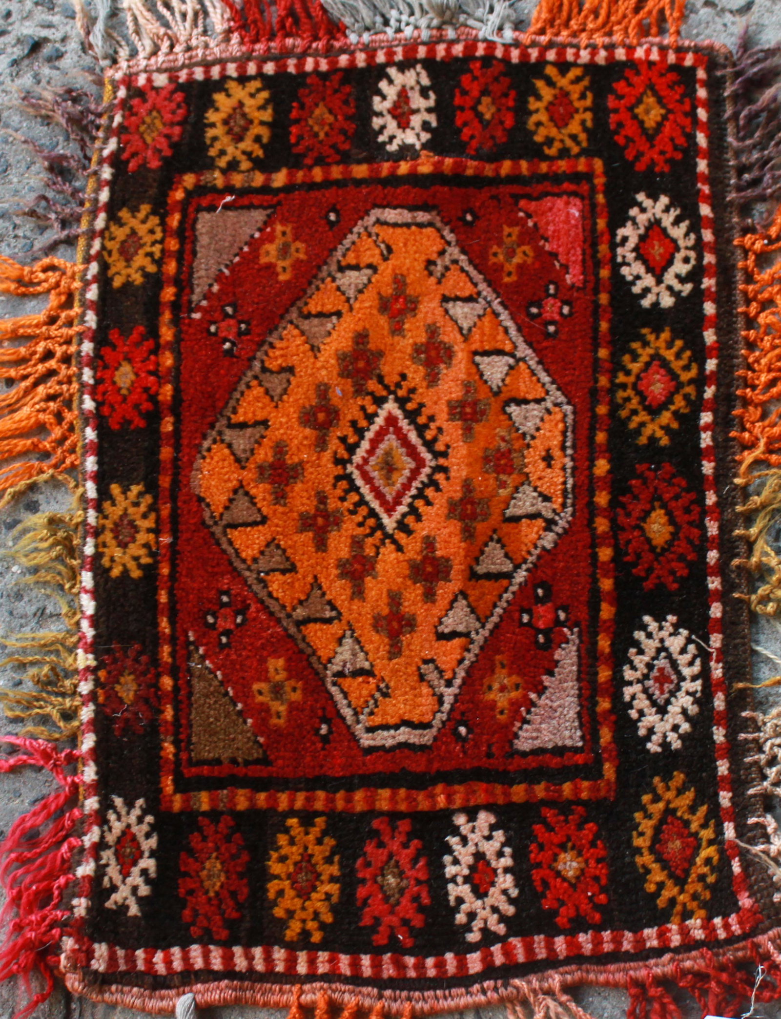 Persian Multi-Color Rug / Mat 1' 8" x 2' 4": Persian Multi-Color Rug / Mat 1' 8" x 2' 4" Persian hand-woven rug / mat with diamond pattern border and center medallion in shades of orange, pink, red, and black. 1' 8" x 2' 4". Minor loss to tassel