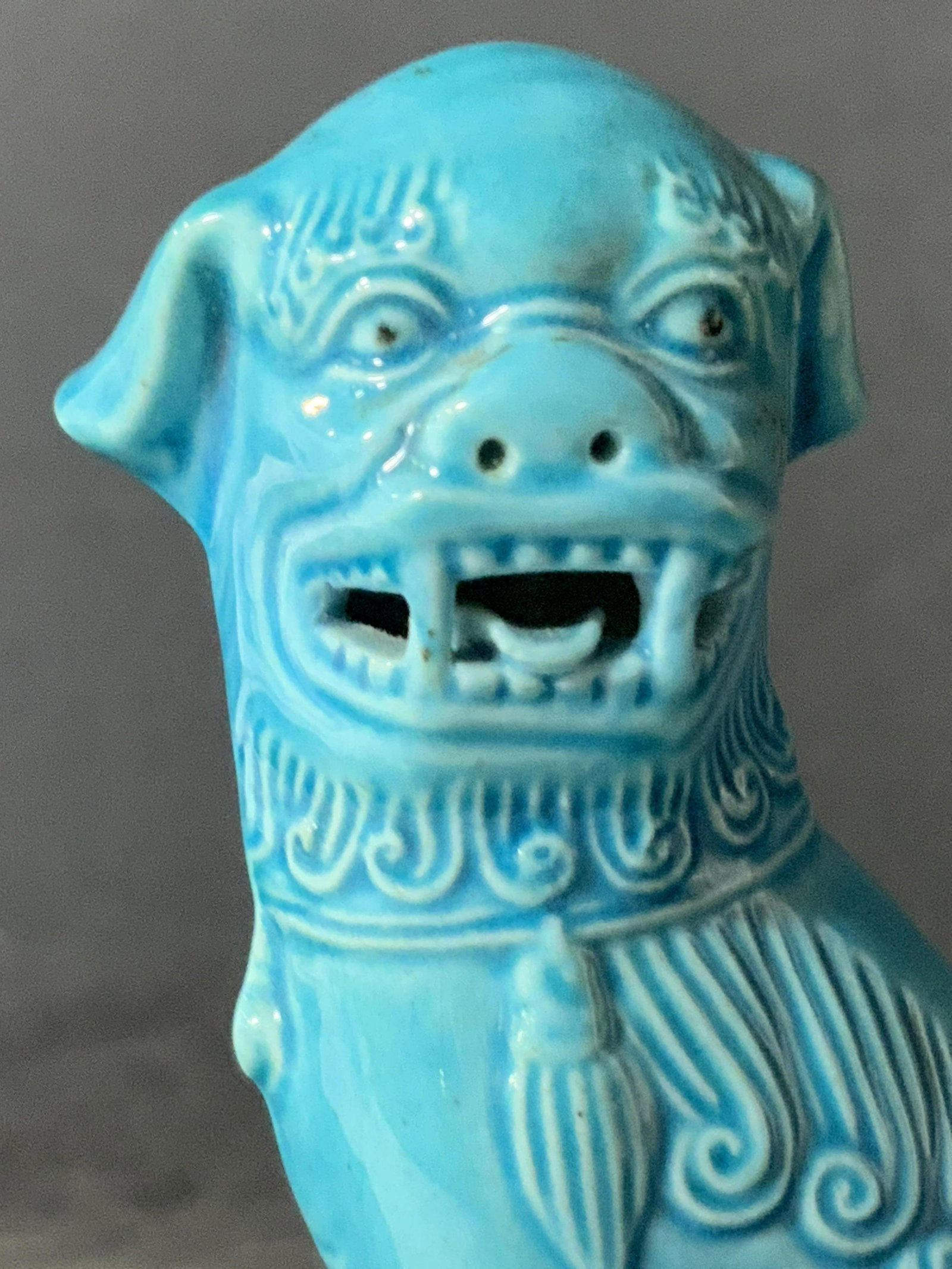 Asian Blue Glazed Porcelain Fu Dog Figural: A porcelain fu dog figural that has been glazed blue. The fu dog sits atop of square base. His mouth is open, tongue lolling out with teeth bared. His paw rests upon a ball. The piece features etched 