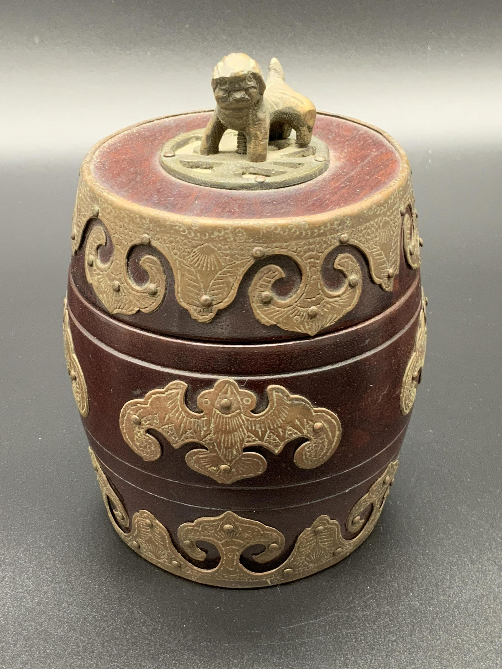 Signed Asian Wood & Metal Barrel W/ Fu Dog Figural: A lidded barrel form vessel crafted from wood and accented with metal decor. The wood is a deep, rich brown. The metals are an antiqued color. Metalwork is etched and embossed. The finial of the lid i