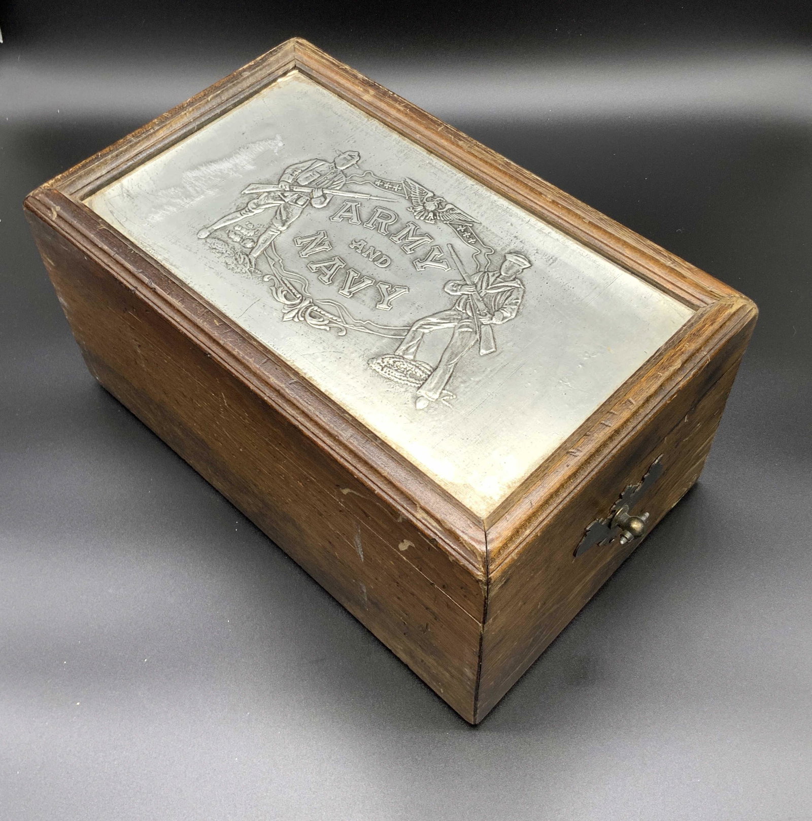 Vintage ARMY & NAVY Wooden Tabletop Keepsake Box: A wooden tabletop keepsake box with a metal, possibly tin, lid accent that reads ARMY AND NAVY. The lid features embossed and etched men holding rifles and wearing tradition military uniforms. piece o