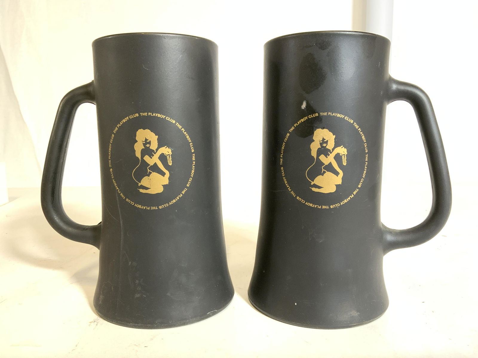 Pair THE PLAYBOY CLUB Female Nude Mug: Lot includes 2 mugs. Each are marked THECPLAYBOY CLUB & depicts female nude figures wearing boots in center. Each are black with gold toned detail. Each piece measures approx 6.5 inches tall 4.5 inche