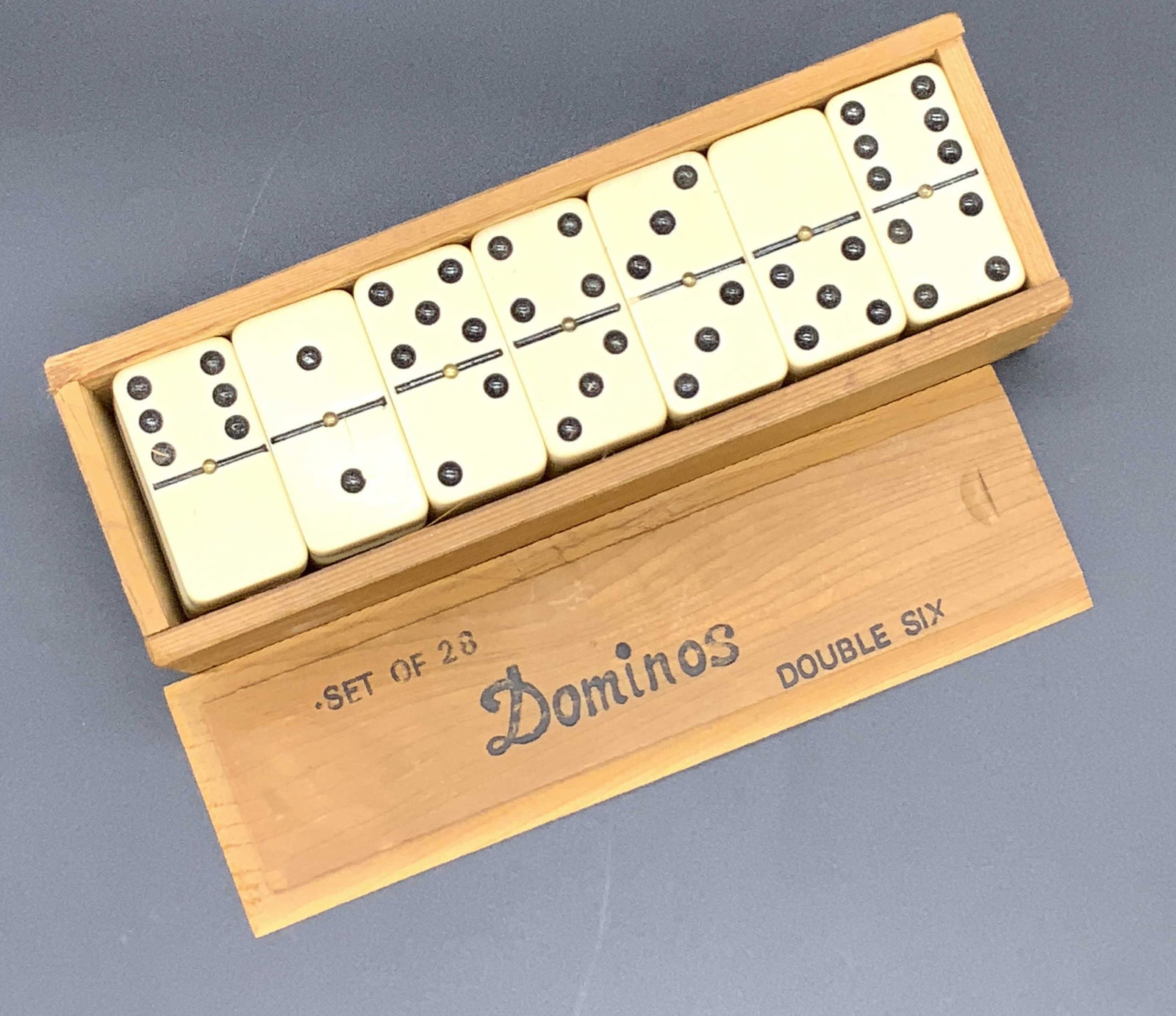 Set 28 DOMINOES Double Six, Tabletop Games: A light brown wooden box containing a set of dominoes. The box lid slides off to reveal the individual game pieces. Lid reads SET OF 28 DOMINOES DOUBLE SIX. Pieces appear to be crafted from plastics, 
