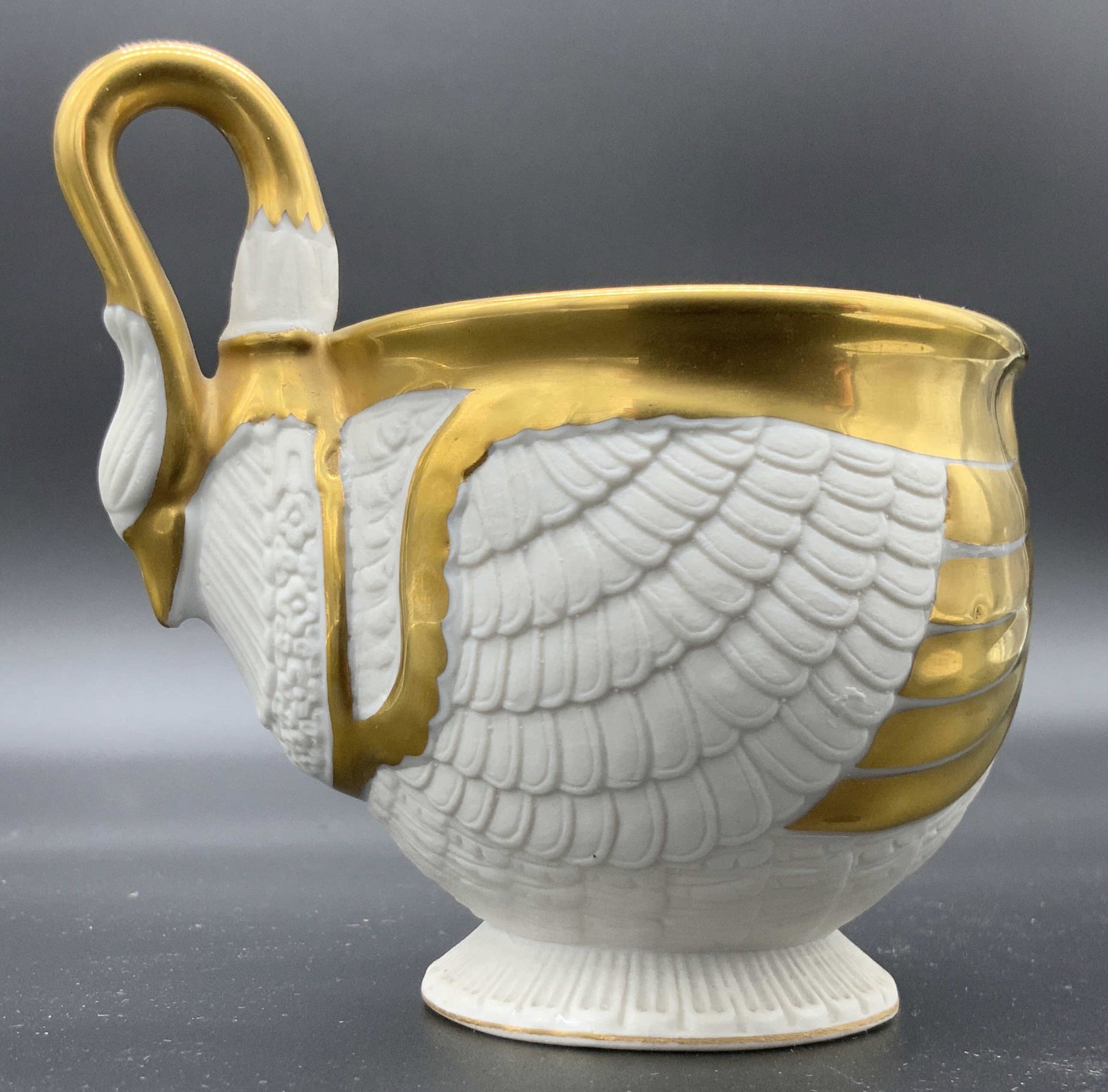 Pair Signed Bavarian Porcelain Saucer & Teacup: A teacup and saucer set crafted from porcelain. The pieces feature embossed white porcelain with gilt accents. The undersides are signed. One piece reads BAVARIA and has a blue anchor stamped on the u