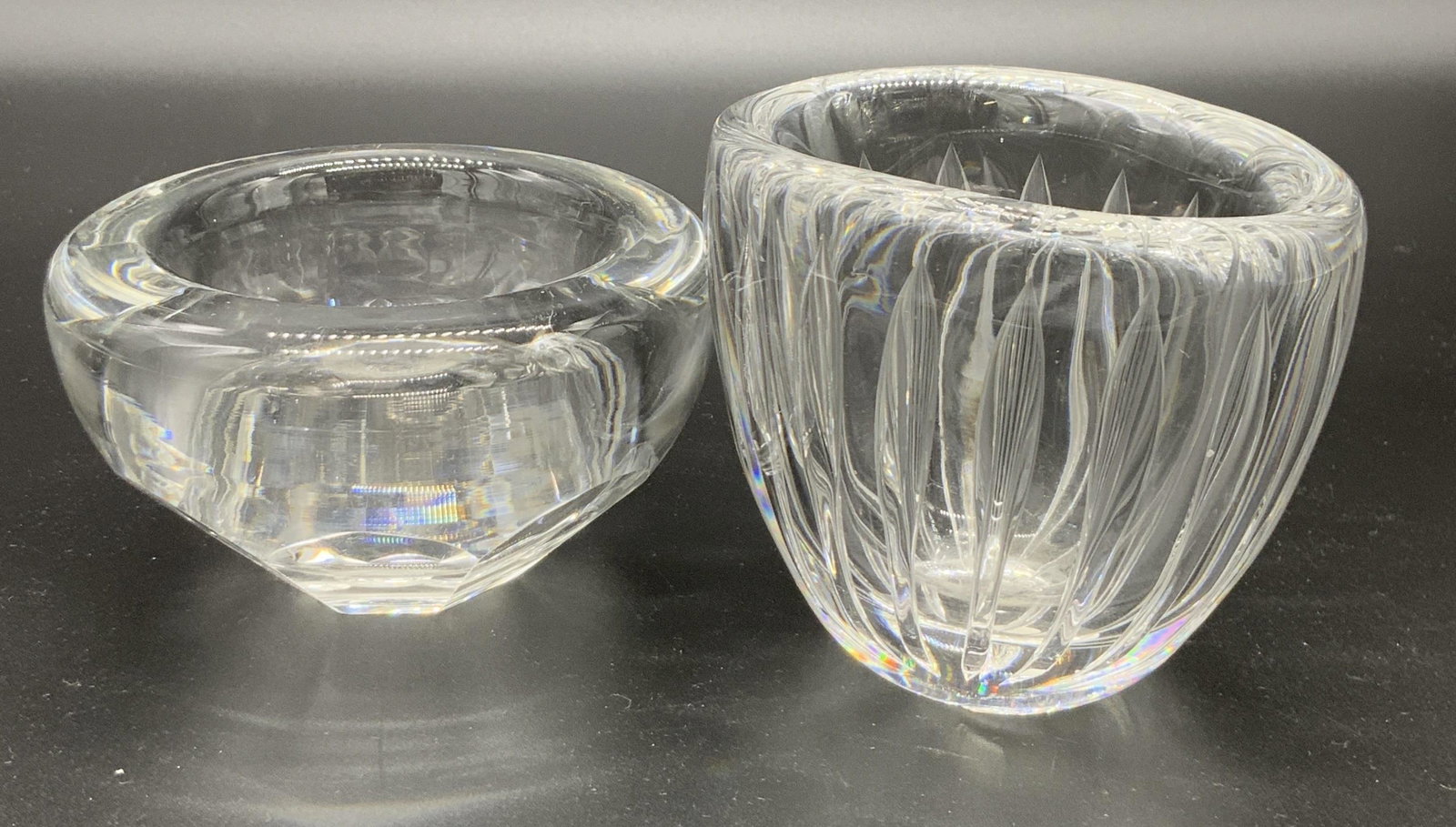 Lot 2 Signed Art Glass Vessels, ORREFORS & More: Two colorless, thick walled glass vessels. Can be used as trinket bowls, keepsake bowls, candy bowls and more. Pieces are weighty. Larger piece approx. 3.5H x 4W in. Larger piece signed LINDSTRAND KOS