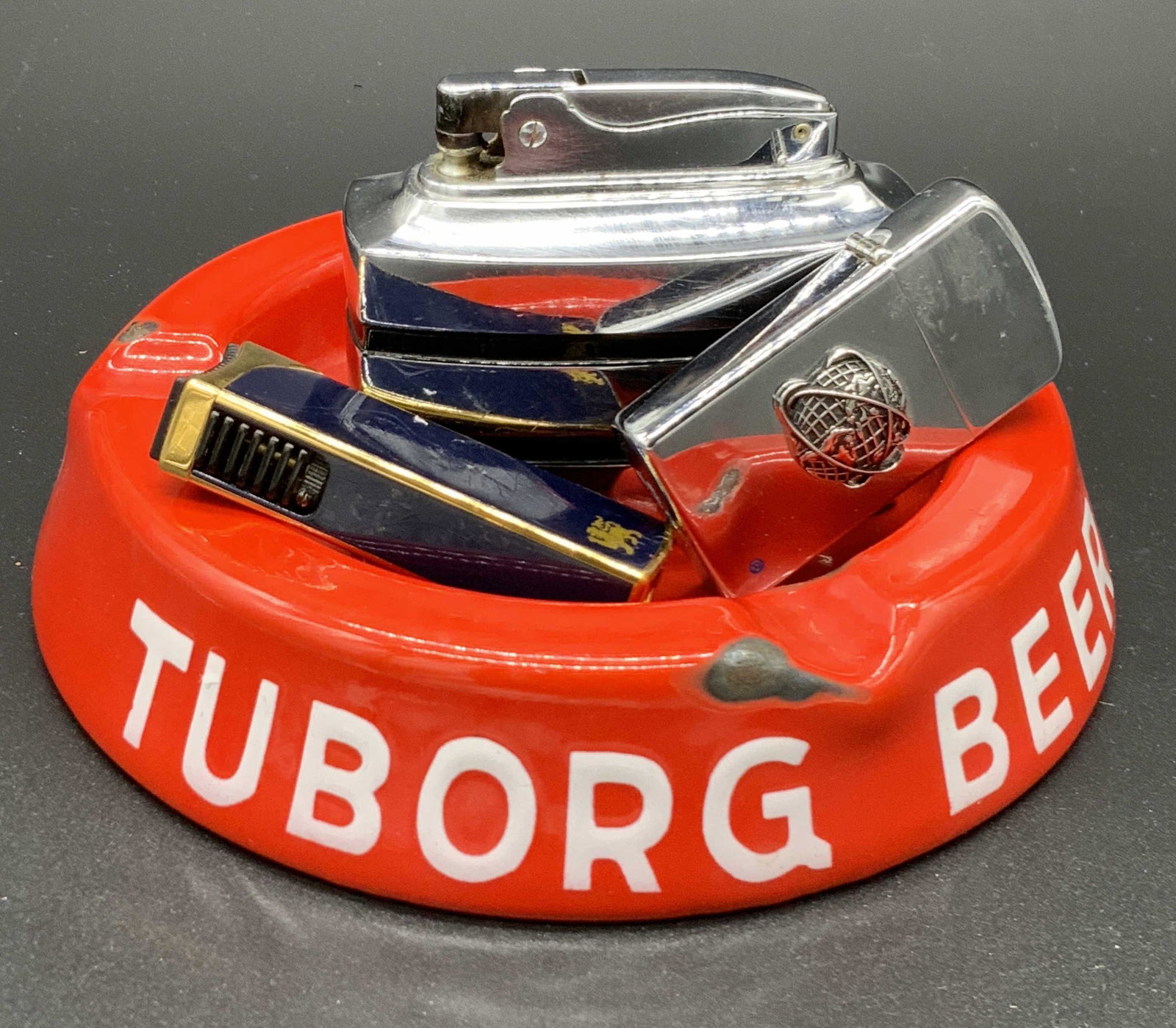 Lot4 Collect Ashtray & Lighters, Vntg ZIPPO & More: One collectible retro red style metal ashtray and three collectible lighters. The ashtray reads MADE IN DENMARK on the underside. Writing in foreign language on the obverse sides. Some wear to metal c