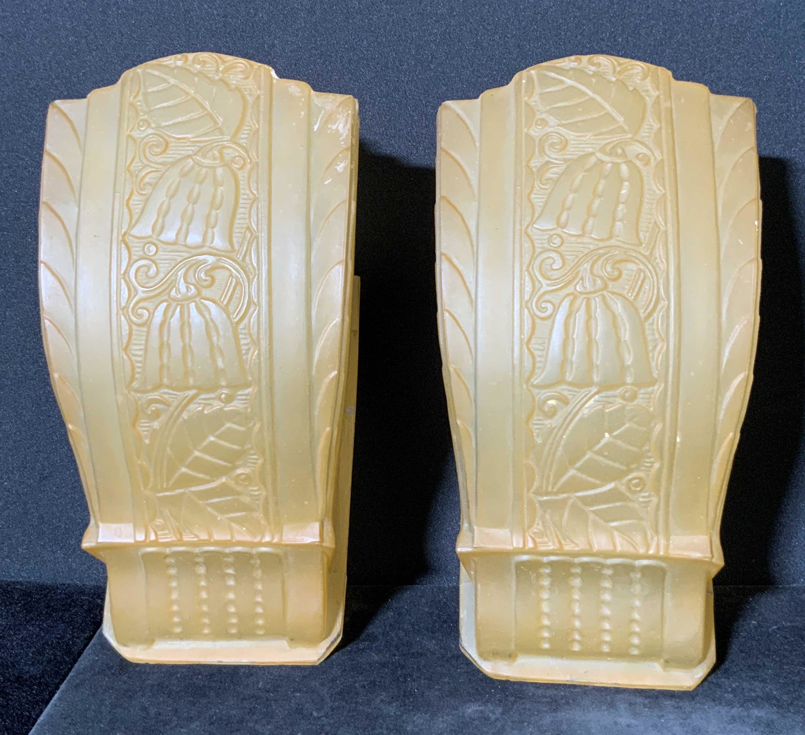 Pair Vintage Art Glass Wall Sconce Covers: Thick walled glass wall sconce covers. Embossed and etched glass designs depict floral motifs. Pieces are a muted orange hue. Pieces possess some chipping. Approx. 7L x 4W in. Art glass, wall sconce c